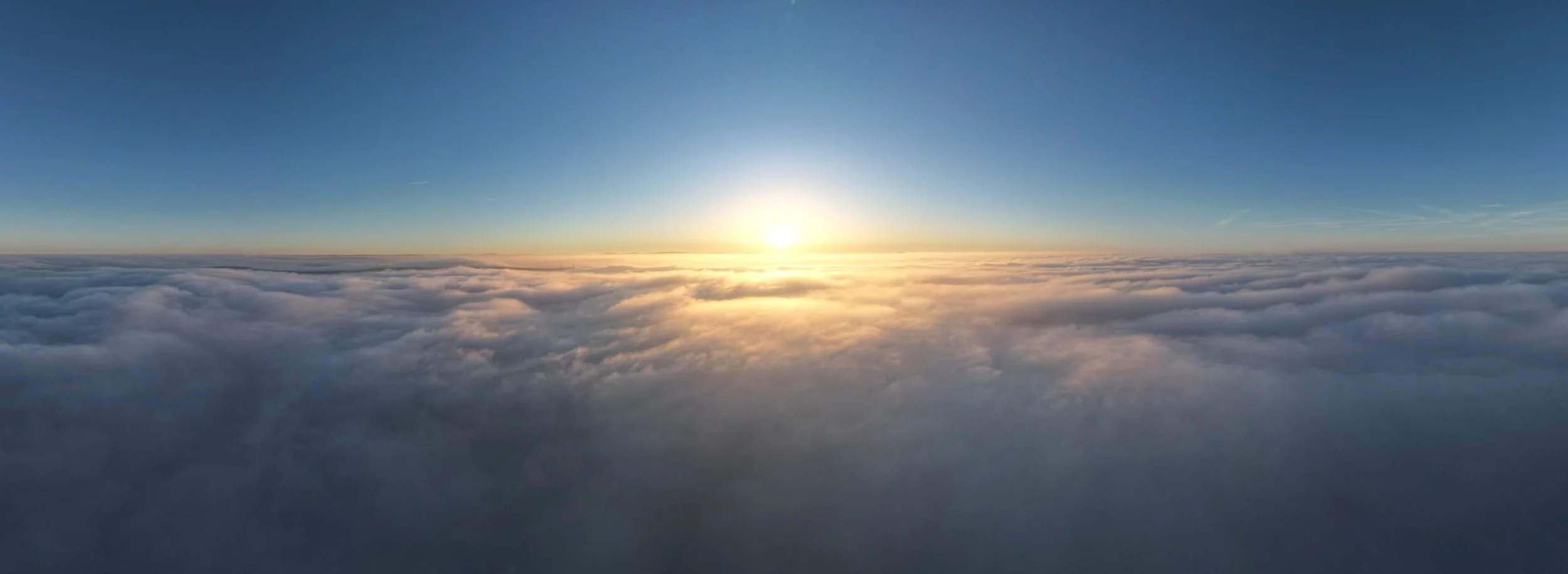 Sunrise above a sea of clouds with a clear blue sky.