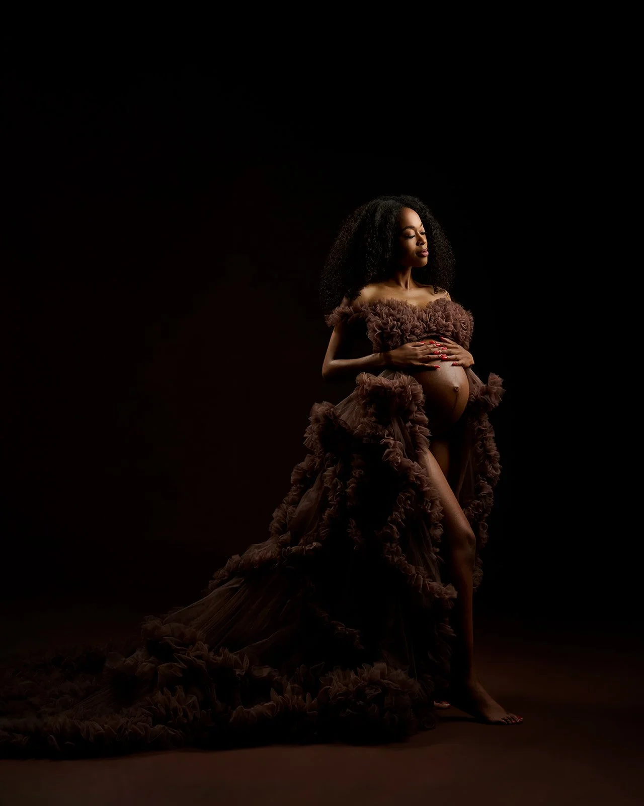 Pregnant woman wearing a dramatic brown ruffled gown in a dark fine-art maternity portrait in Houston