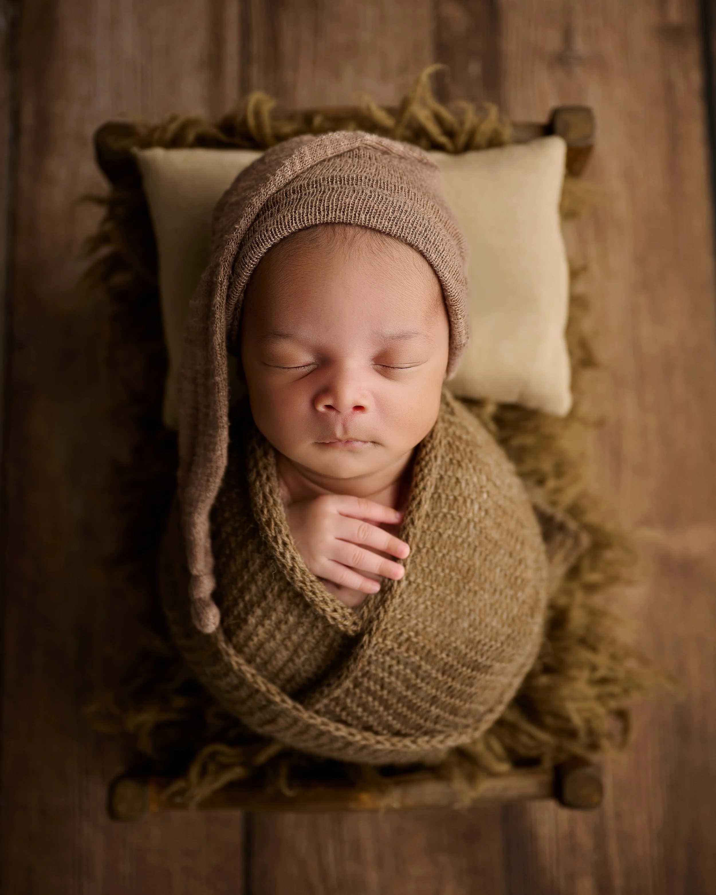 Classic newborn portrait featuring a sleeping baby wrapped in a neutral knit wrap and posed in a rustic wooden bed.