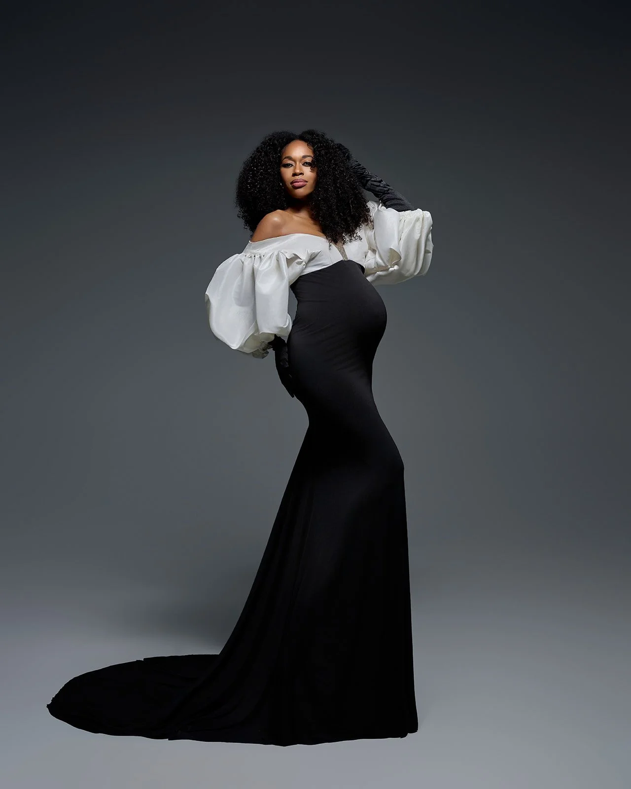 Pregnant woman posing in a fitted black gown with dramatic white sleeves during a Houston studio maternity session.