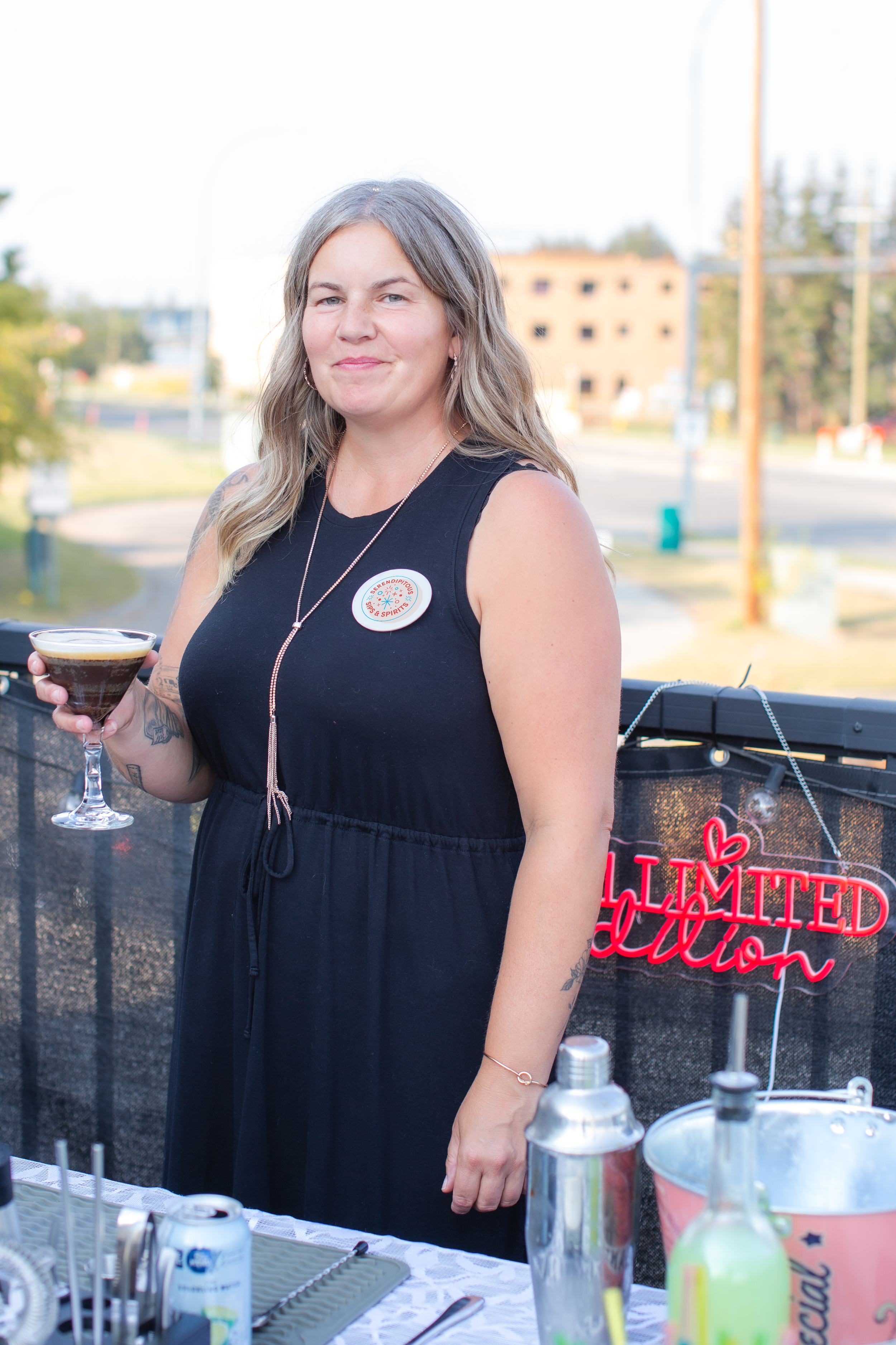 Rosie Silvaggio smiling at the camera while bartending on a rooftop patio with an esspresso martini in hand.