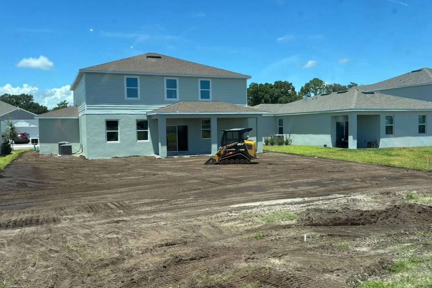 A house under construction with dirt in the yard and a small tracked excavator in the center.