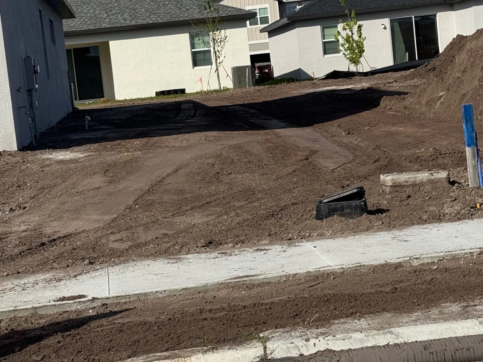 Construction site with dirt ground and partially completed sidewalk in front of modern residential buildings.