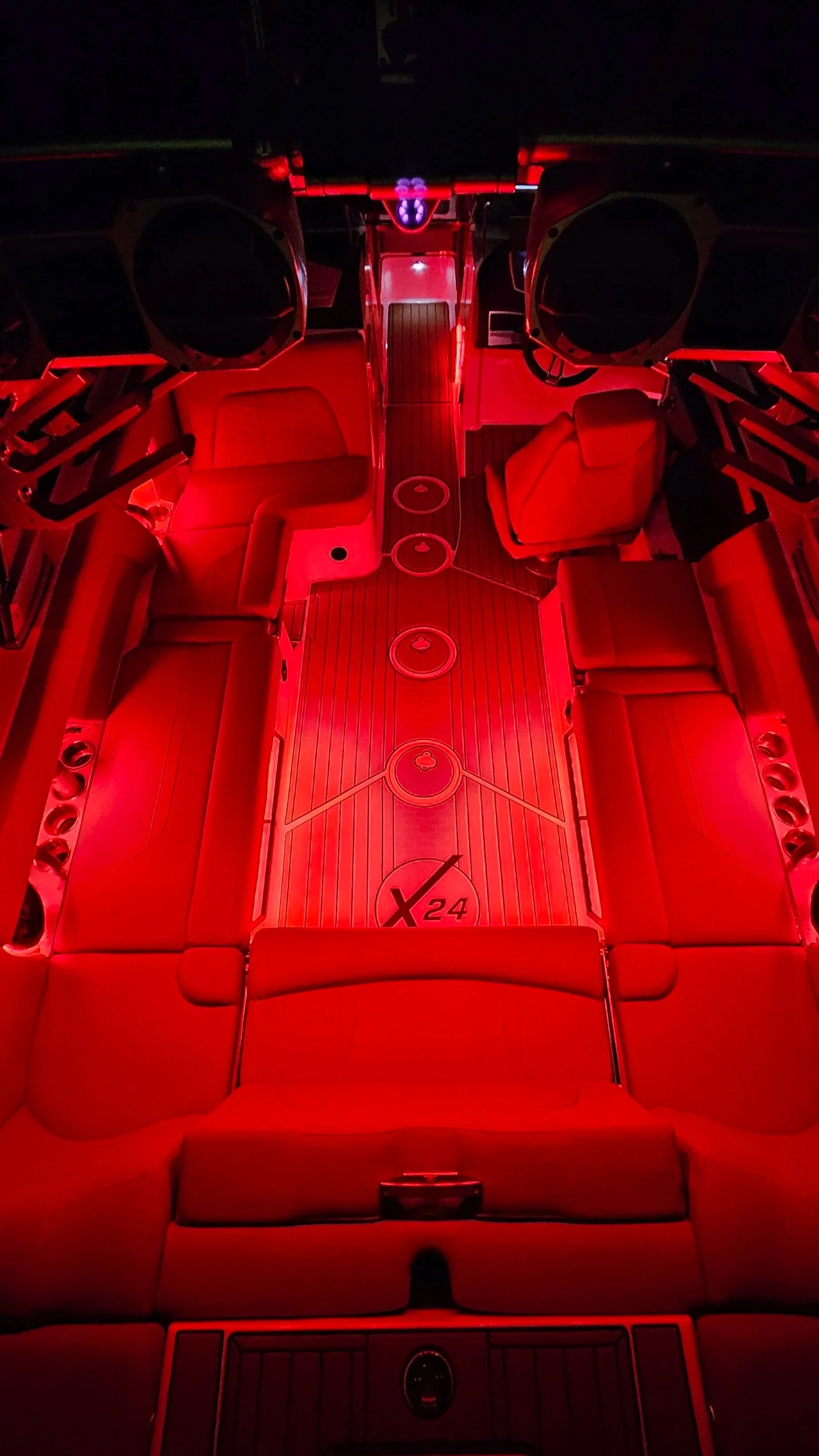 Interior of a luxury vehicle with red lighting, showing multiple seats, a central aisle with drink holders, and high-tech equipment overhead.