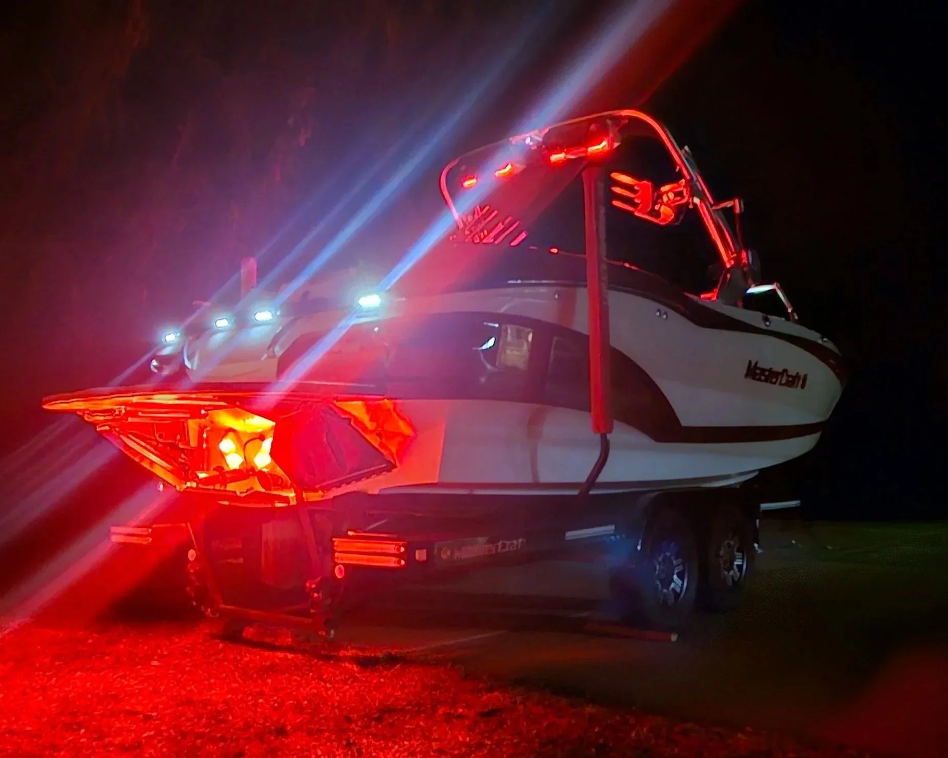 A boat on a trailer at night with red and white LED lights illuminating it.