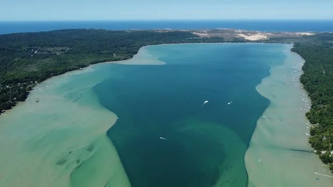 Aerial view of a beach with clear shallow waters and green forest on both sides.