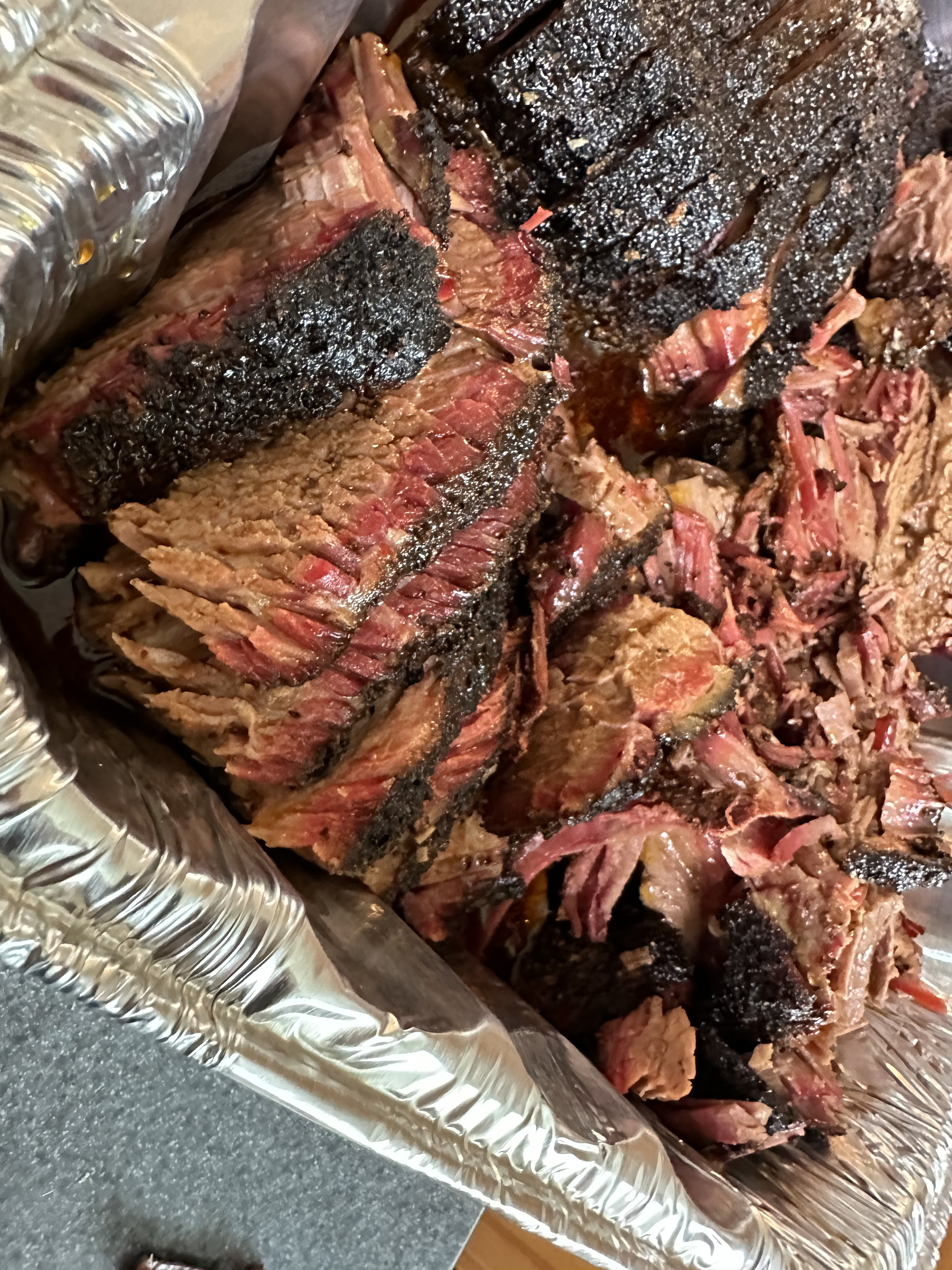 Cooked smoked beef brisket meat with a dark bark crust, sliced and shredded on aluminum foil.