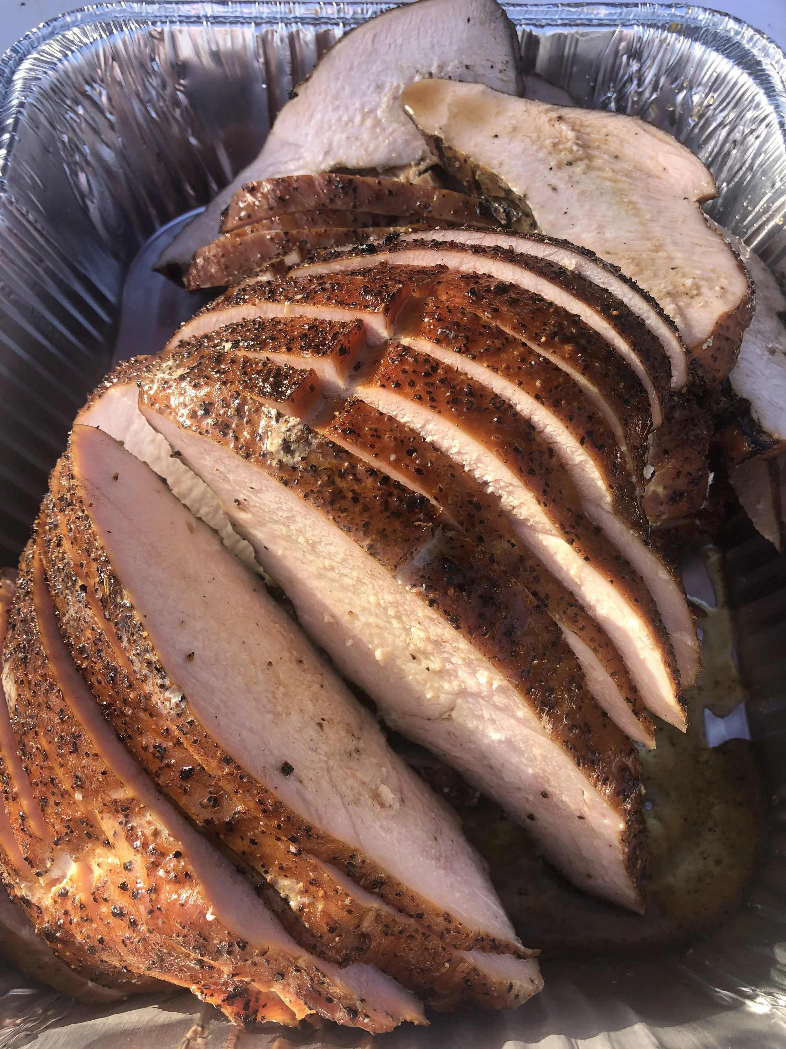 Slices of cooked turkey breast with seasoned, crispy skin in a metal serving tray.