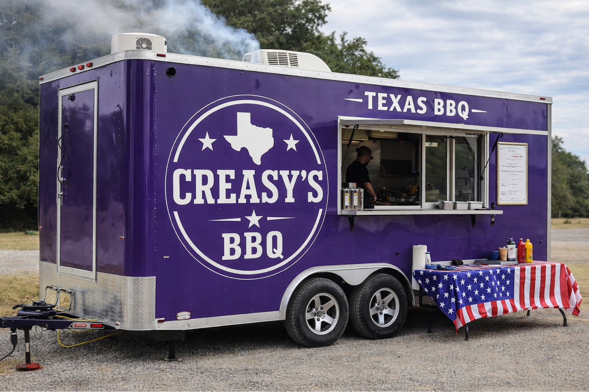 A purple Texas BBQ food truck with 'Creasy's BBQ' logo, featuring an outline of Texas and stars. The truck has a window with a person inside preparing food. A table outside is covered with an American flag tablecloth and condiments.