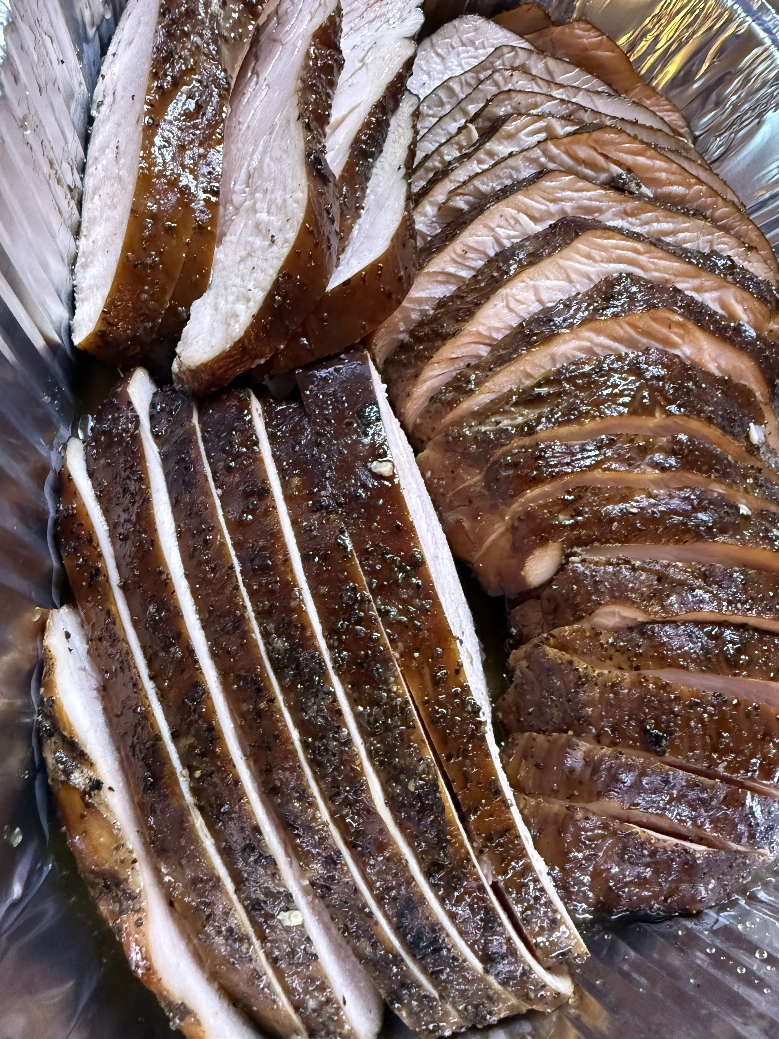 Sliced smoked or cured meat, possibly salmon or pork, arranged in a container.