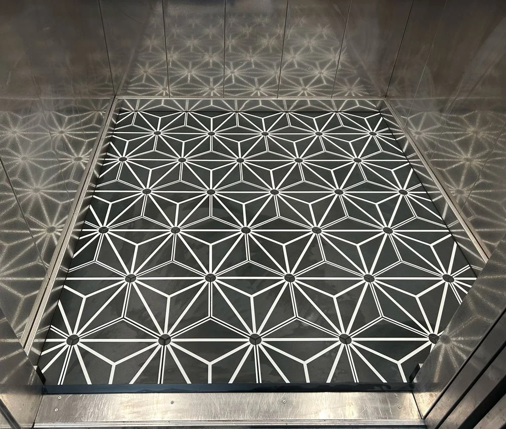 Patterned black and white floor with geometric design, inside an elevator with reflective metal walls.