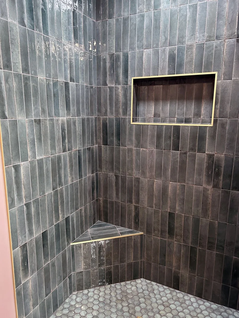 Interior of a tiled shower with a recessed shelf and a corner seat, all covered in dark green tiles.