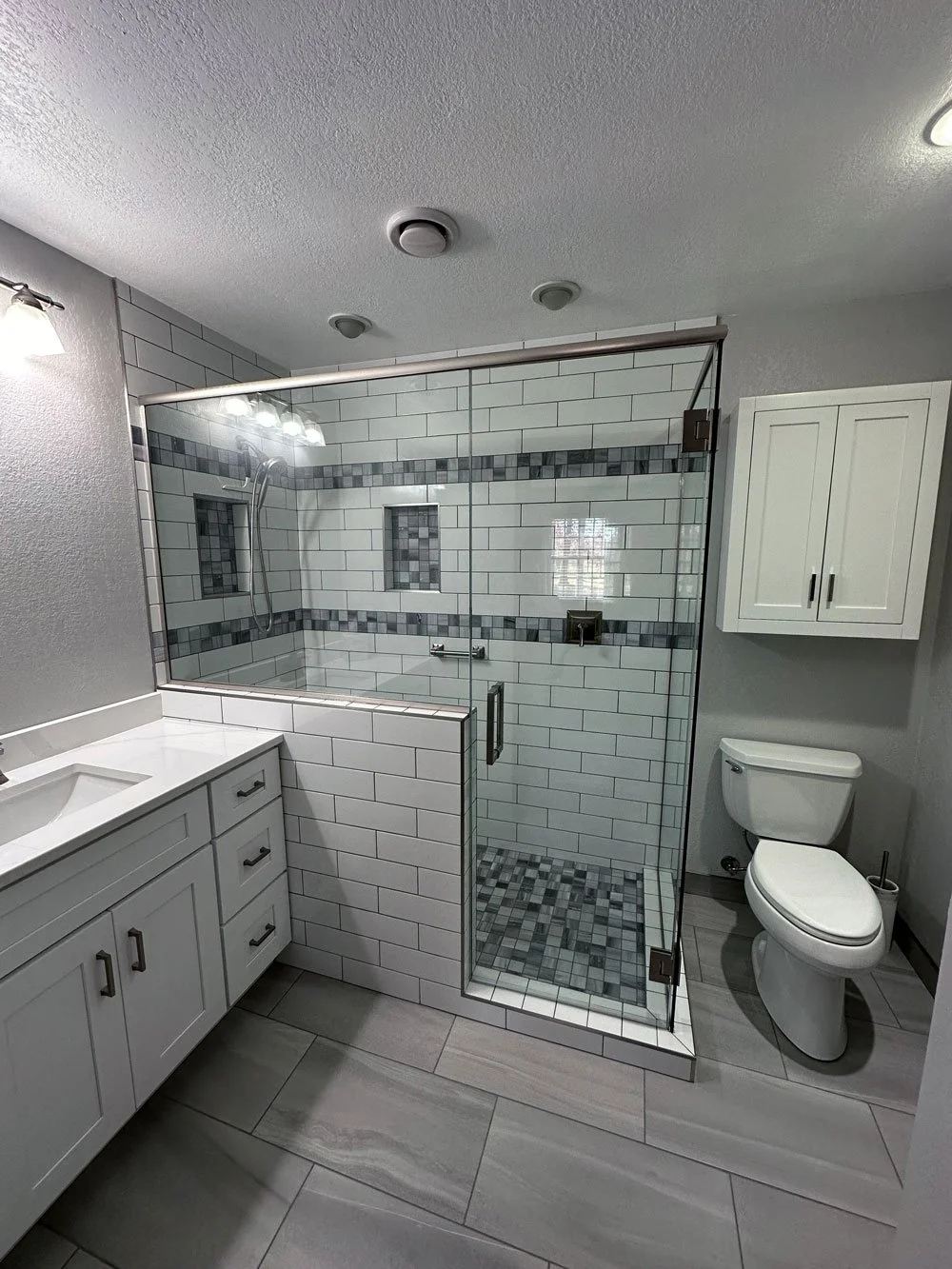 Clean, modern bathroom with a glass-enclosed shower, white cabinets, and a toilet, all with neutral gray and white tones.
