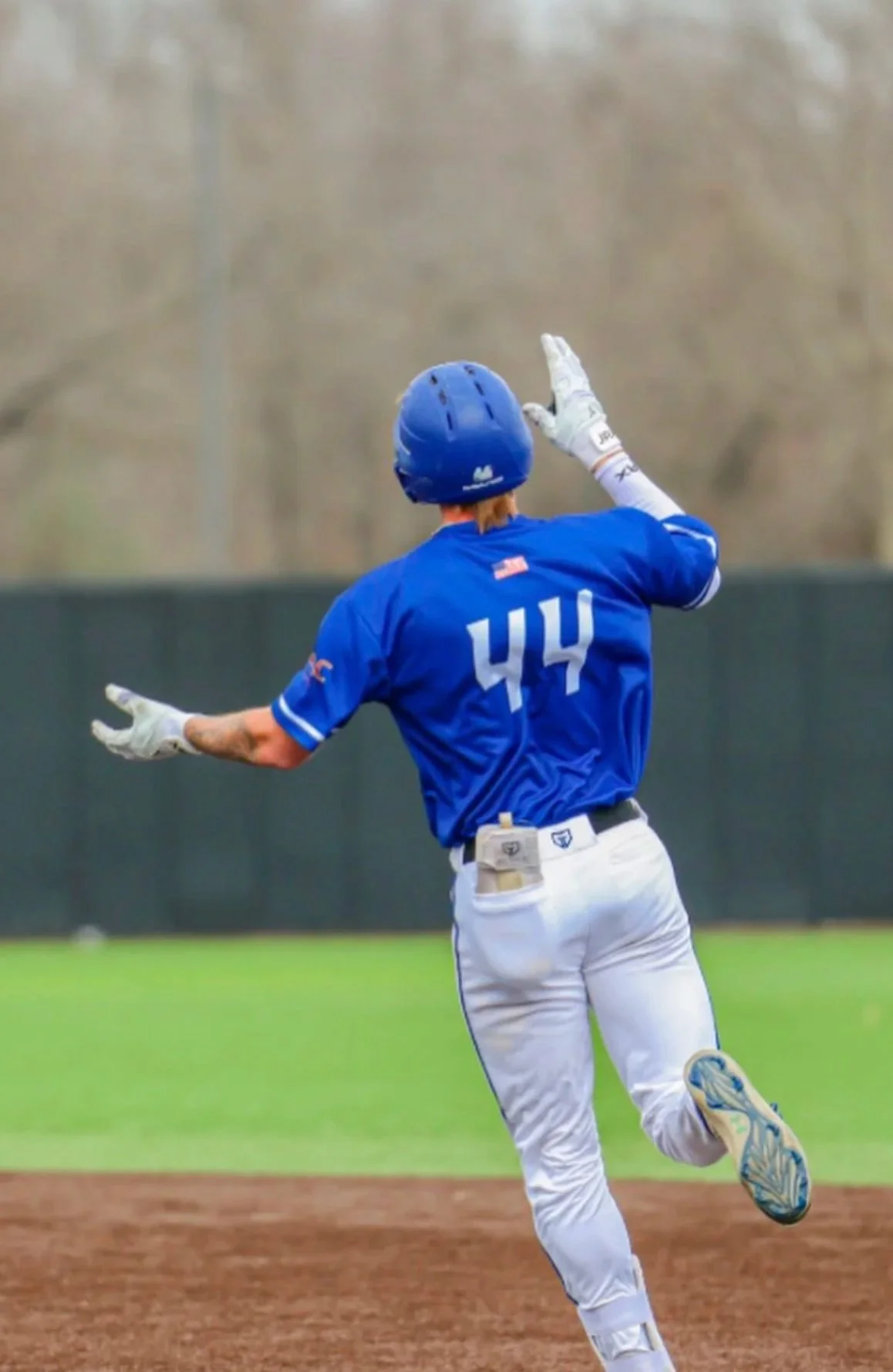 A baseball player wearing a blue jersey with the number 44, white pants, and a blue helmet, running on a baseball field with arms outstretched.