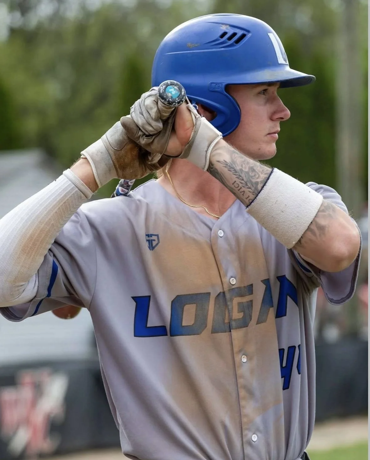 A baseball player wearing a blue helmet and gray uniform with 'Logan' written on it, holding a bat over his shoulder, preparing to bat.