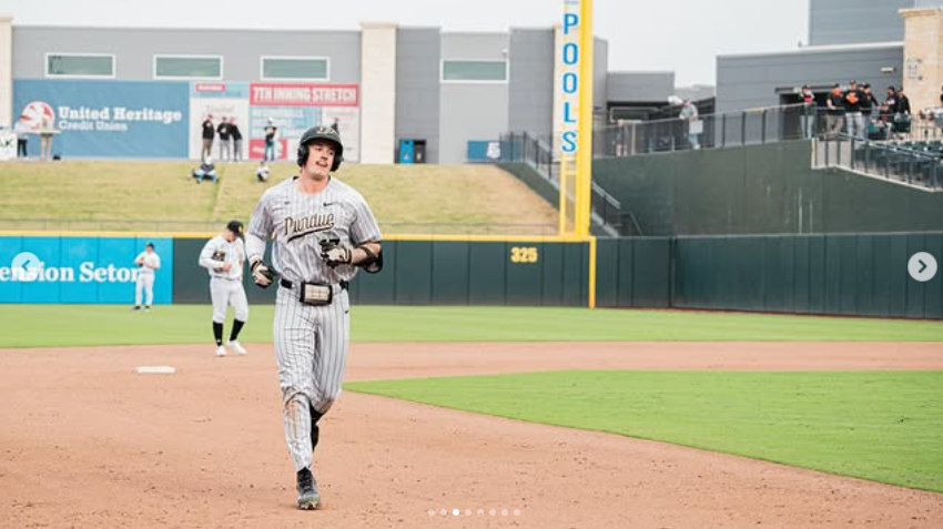 A baseball player runs on the field during a game at a stadium, with spectators and other players visible in the background.