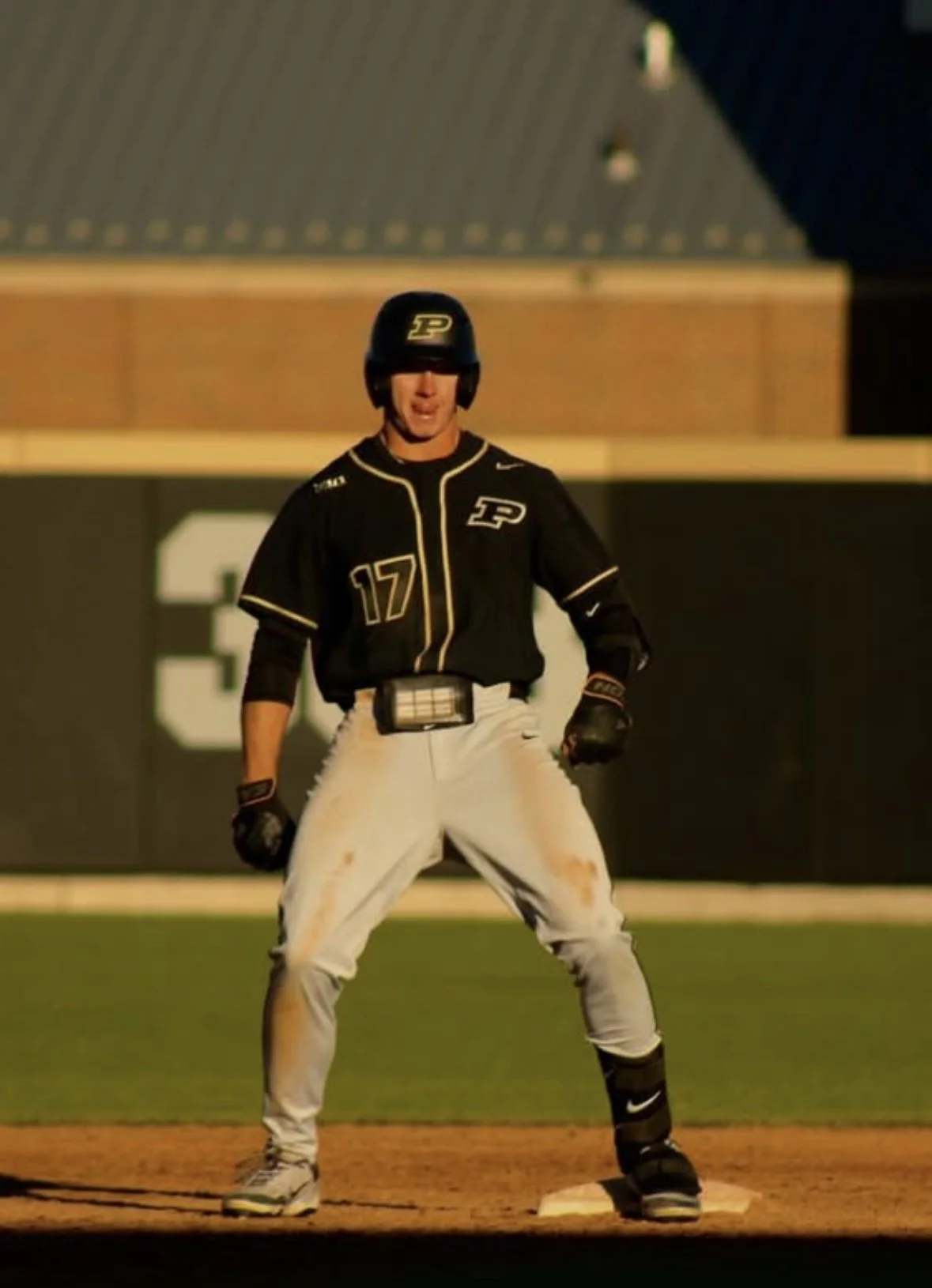 A baseball player in a black and white uniform stands on a base on the field during a game at night. He is wearing a helmet, gloves, and cleats, with a Pittsburgh Pirates logo visible.