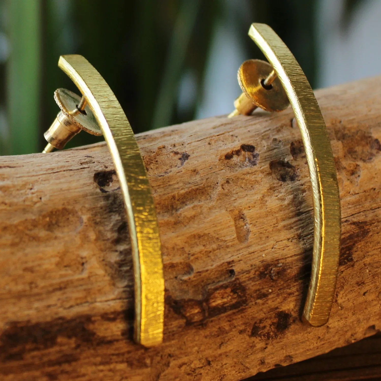 Close-up of gold earrings resting on a piece of wood.