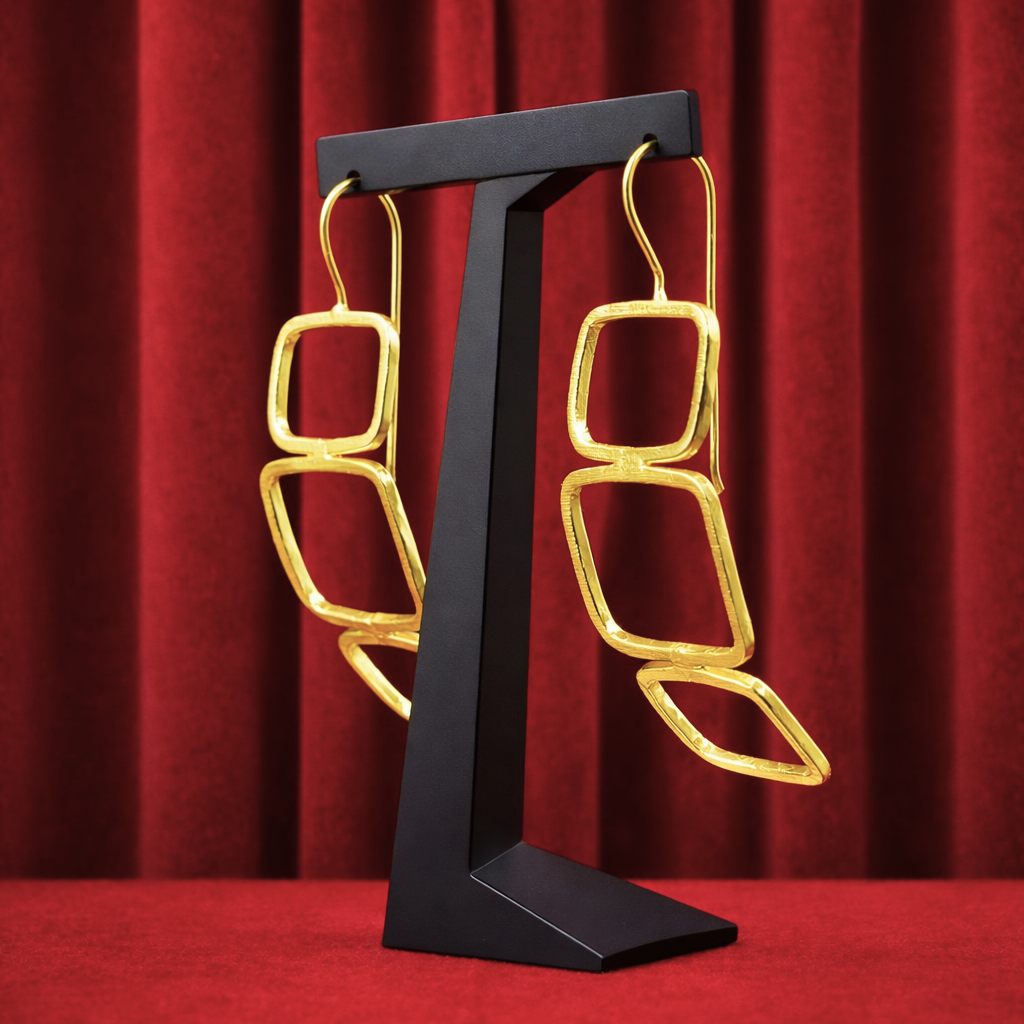 Gold geometric earrings hanging on a black display stand against a red velvet background.
