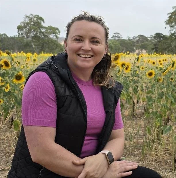 a picture of Brooke sitting in front of a field of sunflowers