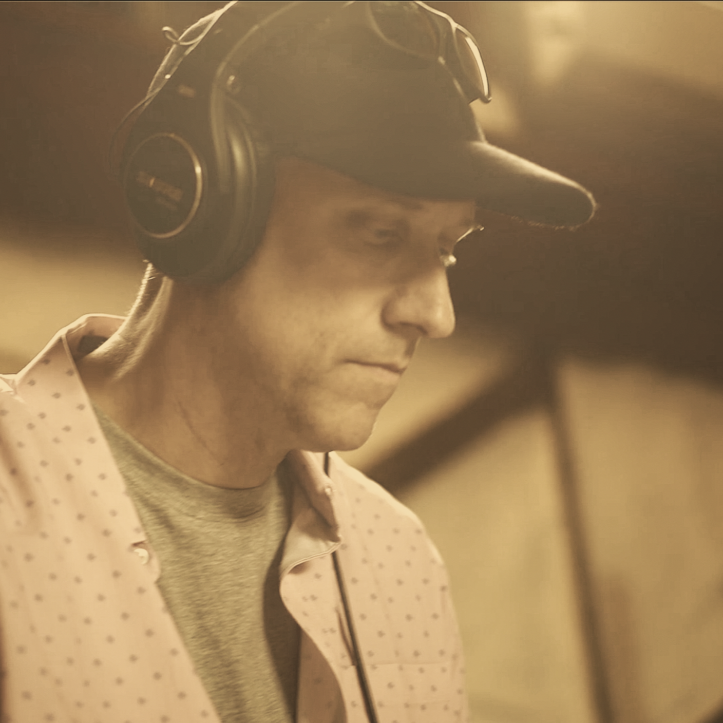 A young man wearing headphones and a baseball cap looks down thoughtfully.