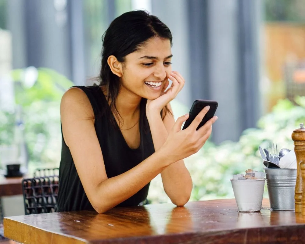 A woman smiling at her phone providing feedback on the proposed Menangle Park Woolworths development.
