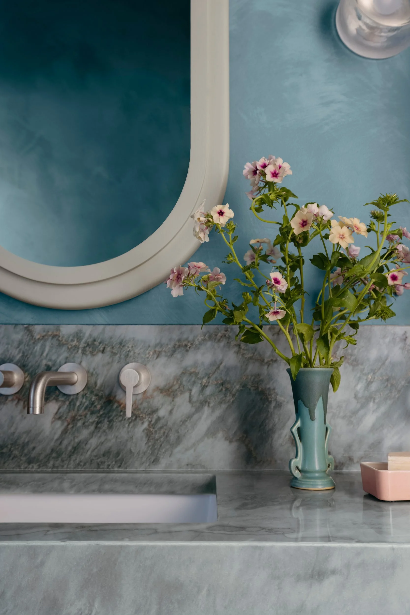 Floating stone vanity with a wall-mounted faucet and pink flowers in the teal and mint green powder room