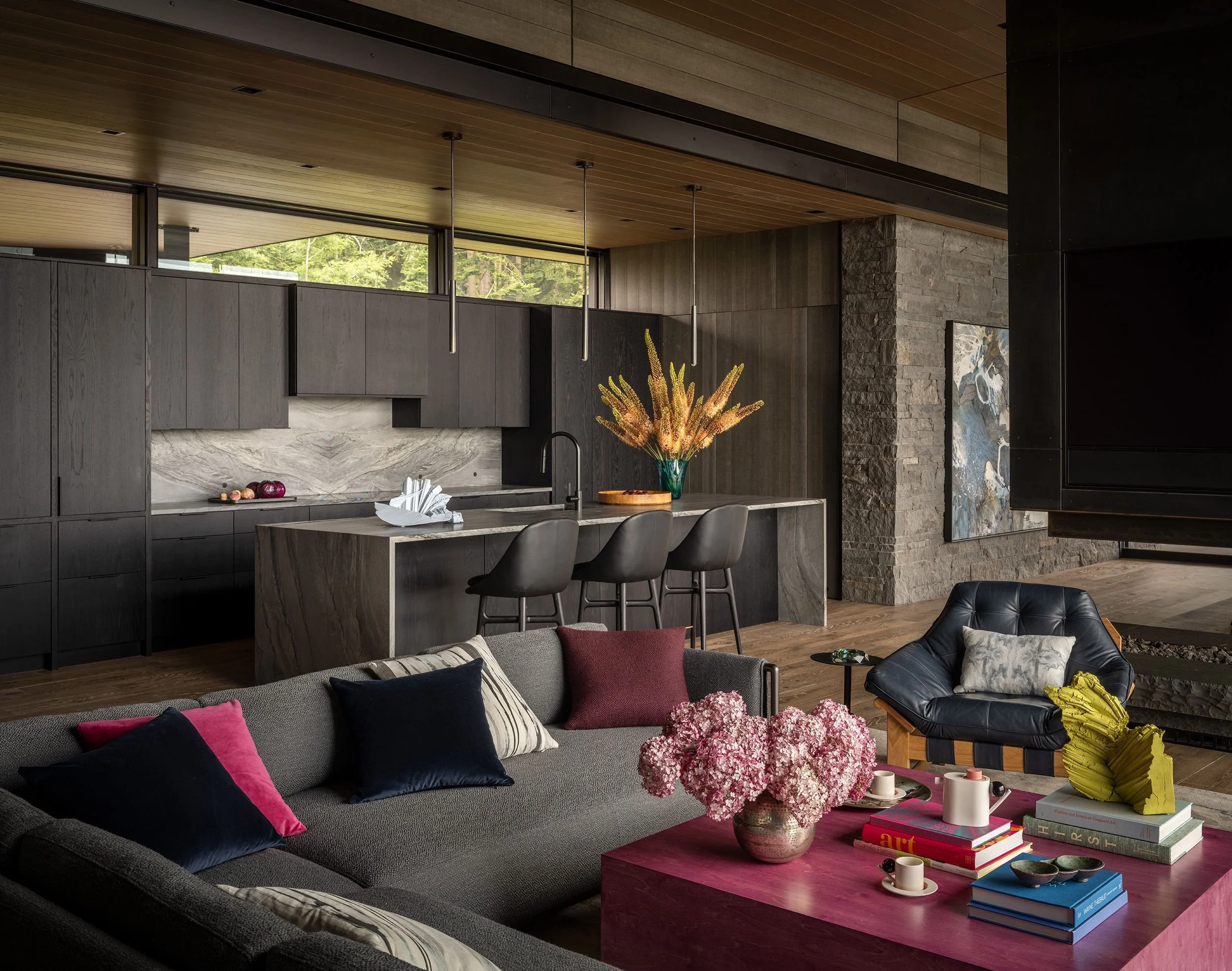 Open living room and kitchen in a Whidbey Island home, with a charcoal sectional, a magenta coffee table and dark oak kitchen cabinetry