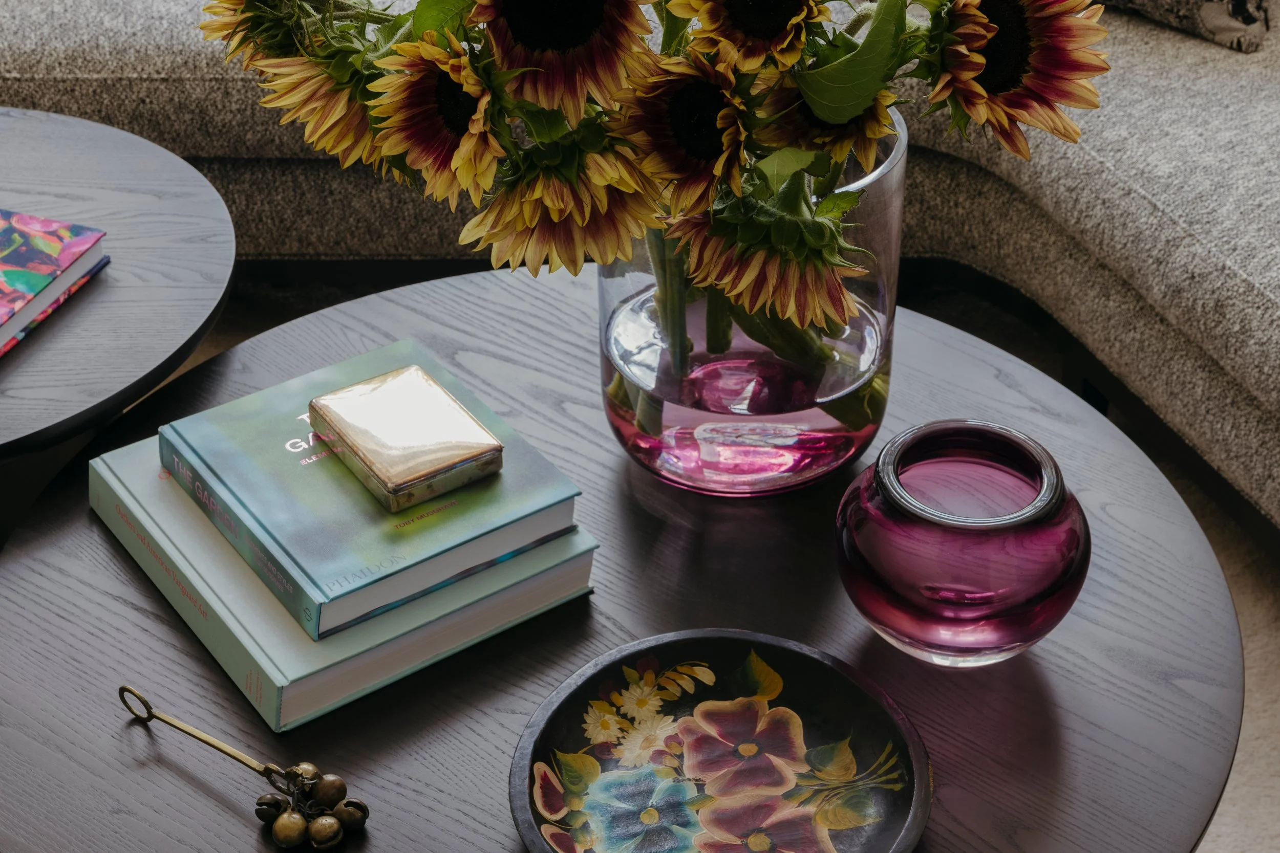 Coffee table styled with books, a purple glass vase of sunflowers and a painted floral dish