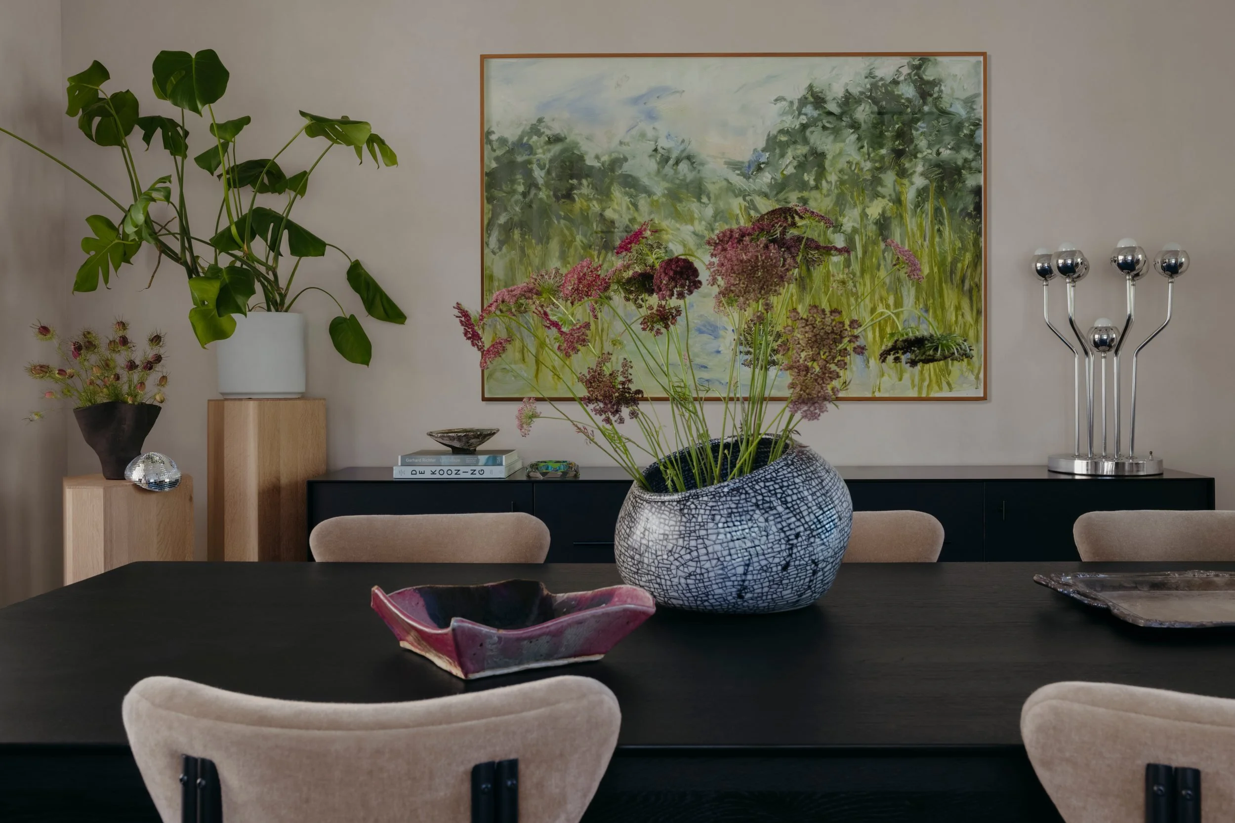 Black-stained oak dining table and black and steel buffet below a soft floral abstract painting by Mya Kerner