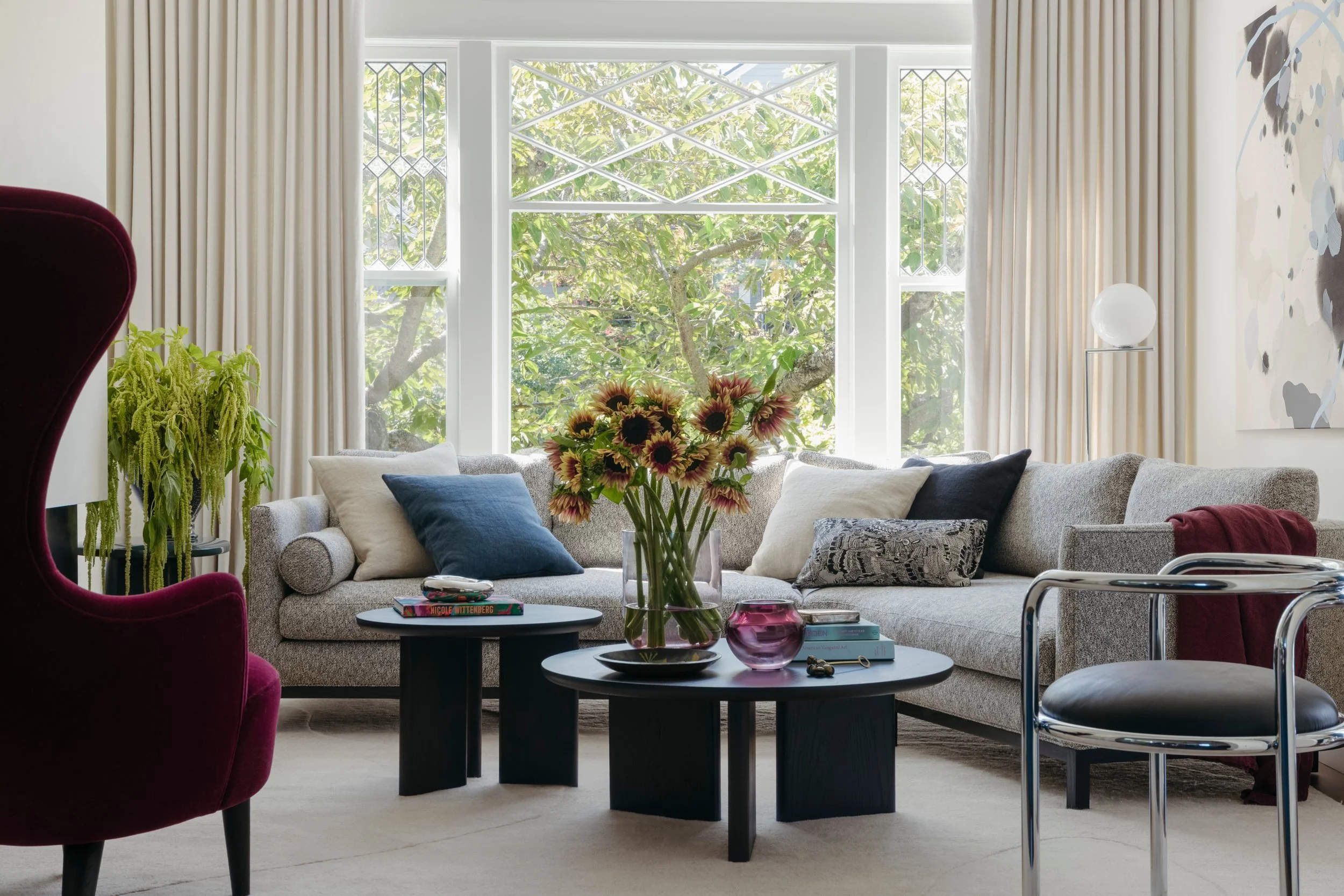 Living room with a burgundy wing chair, a chrome and black leather chair, a gray sofa and two round black coffee tables