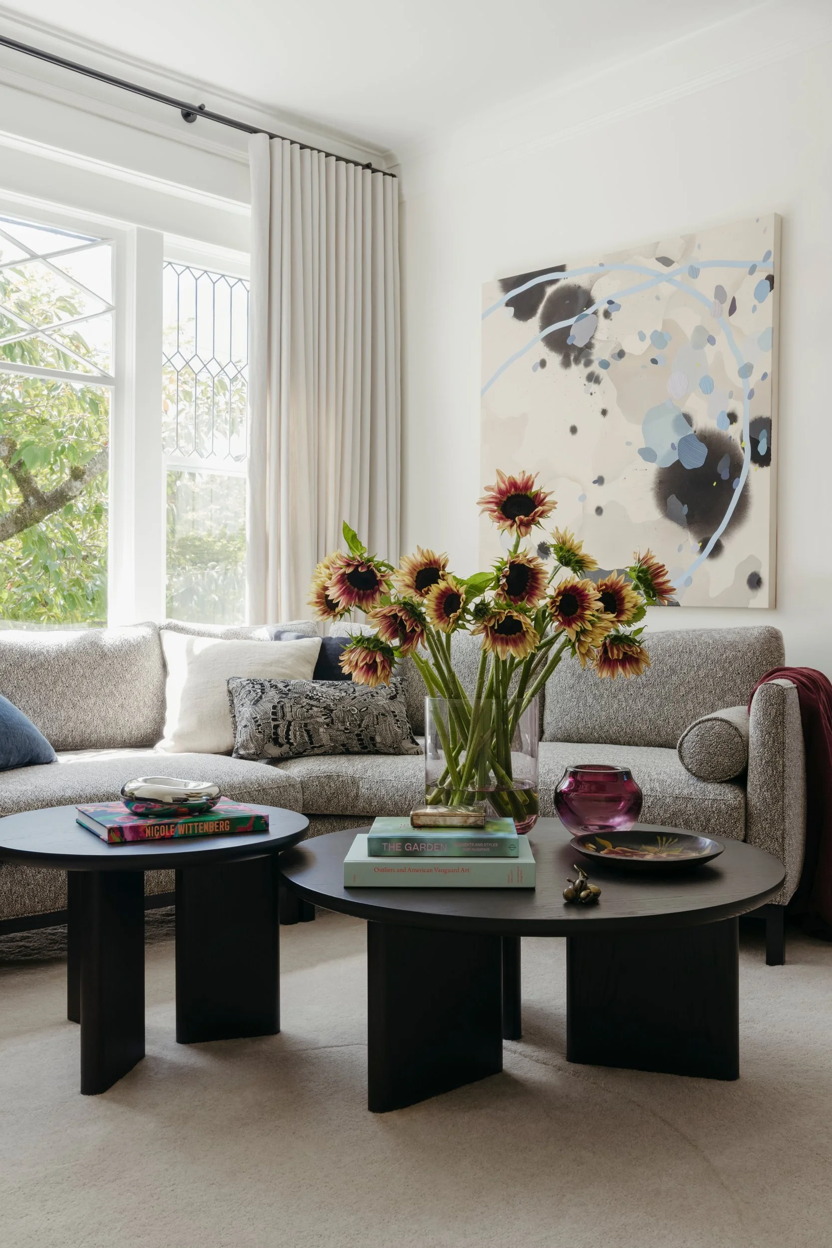 Living room with a playful modern painting above a gray sofa, round black coffee tables and sunflowers