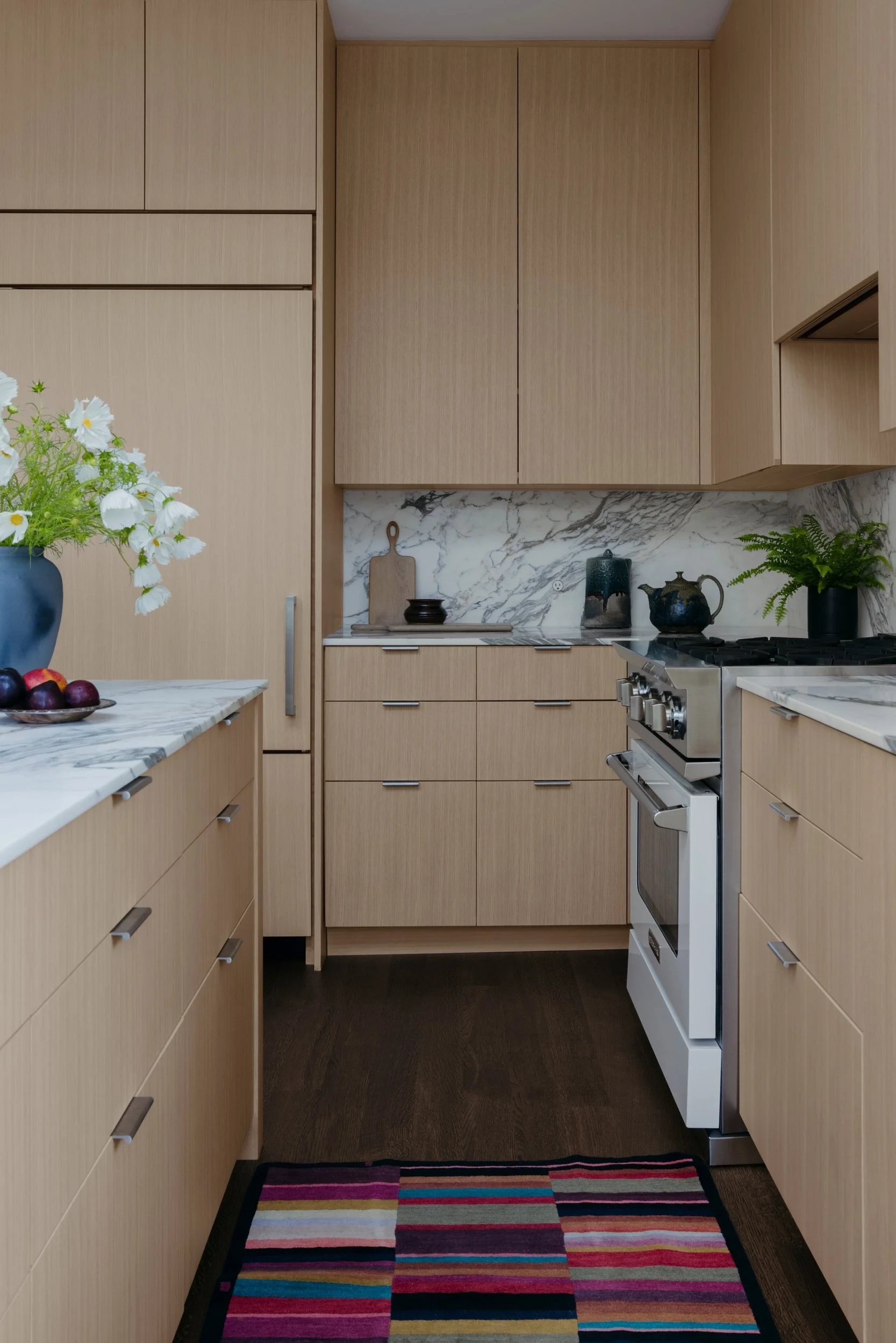 Kitchen with light oak cabinetry, a marble backsplash and a colorful striped runner