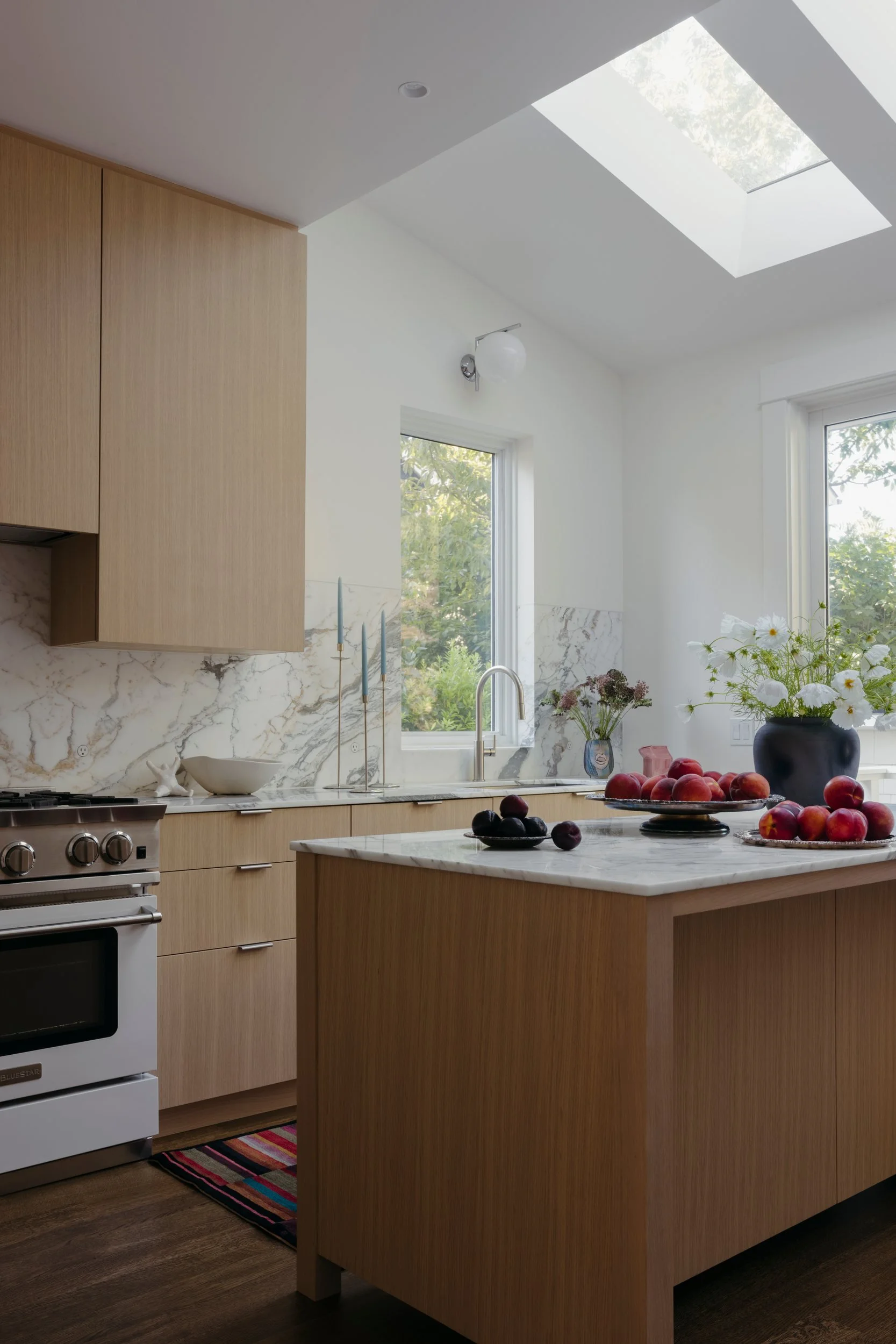 Kitchen island under a skylight, with light oak cabinetry and a marble backsplash