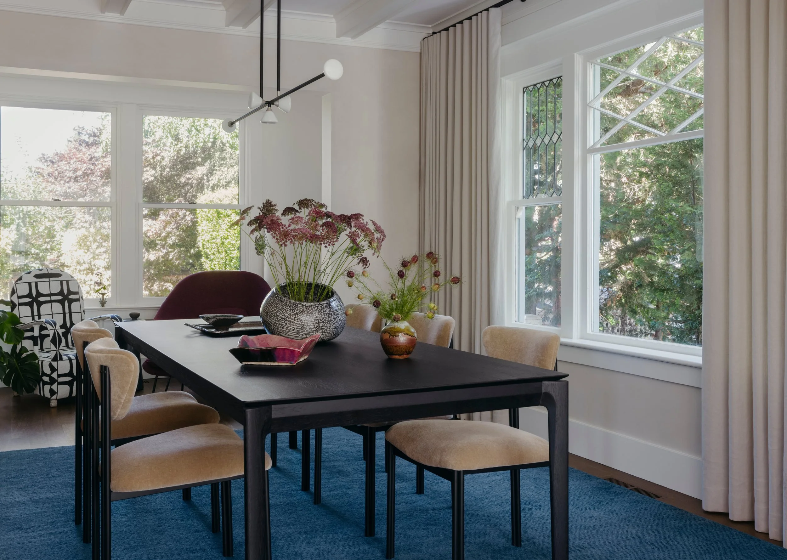Dining room with a dark blue-gray rug, a black-stained oak table and black steel chairs in beige mohair