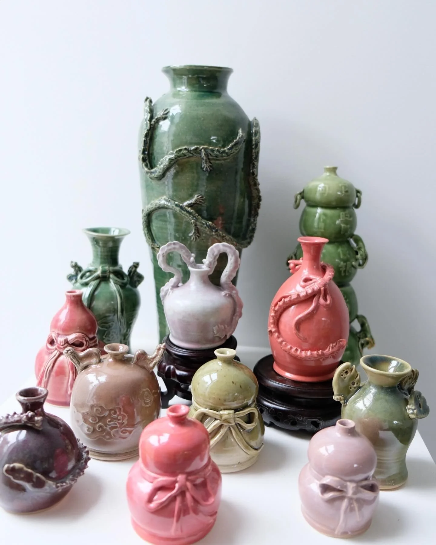 Collection of ceramic vases and jars in various shapes, sizes, and colors, some with intricate designs and decorative details, displayed on a white surface against a plain background.