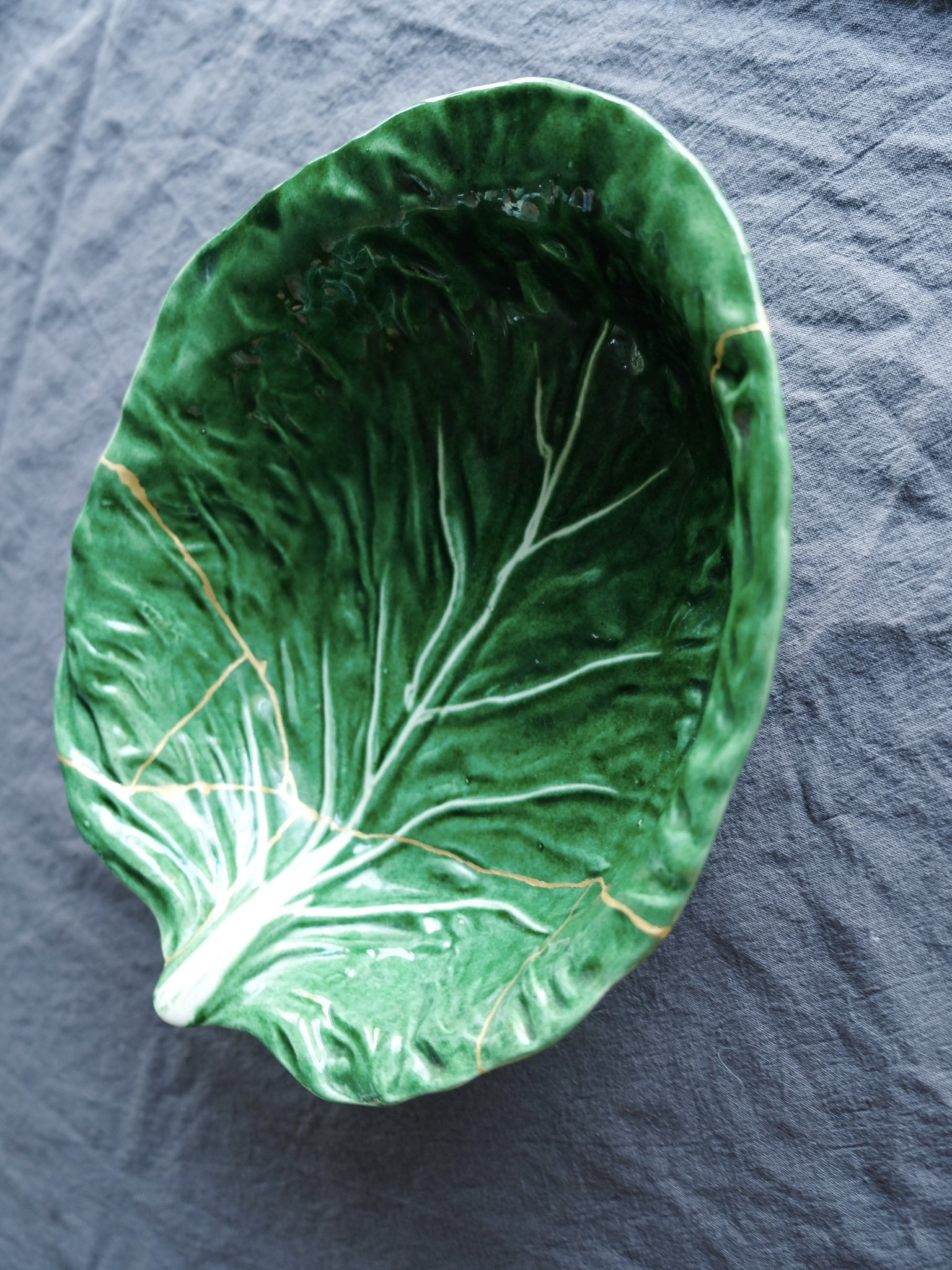 Green ceramic dish shaped like a leaf with white and gold veins, placed on a dark fabric surface.