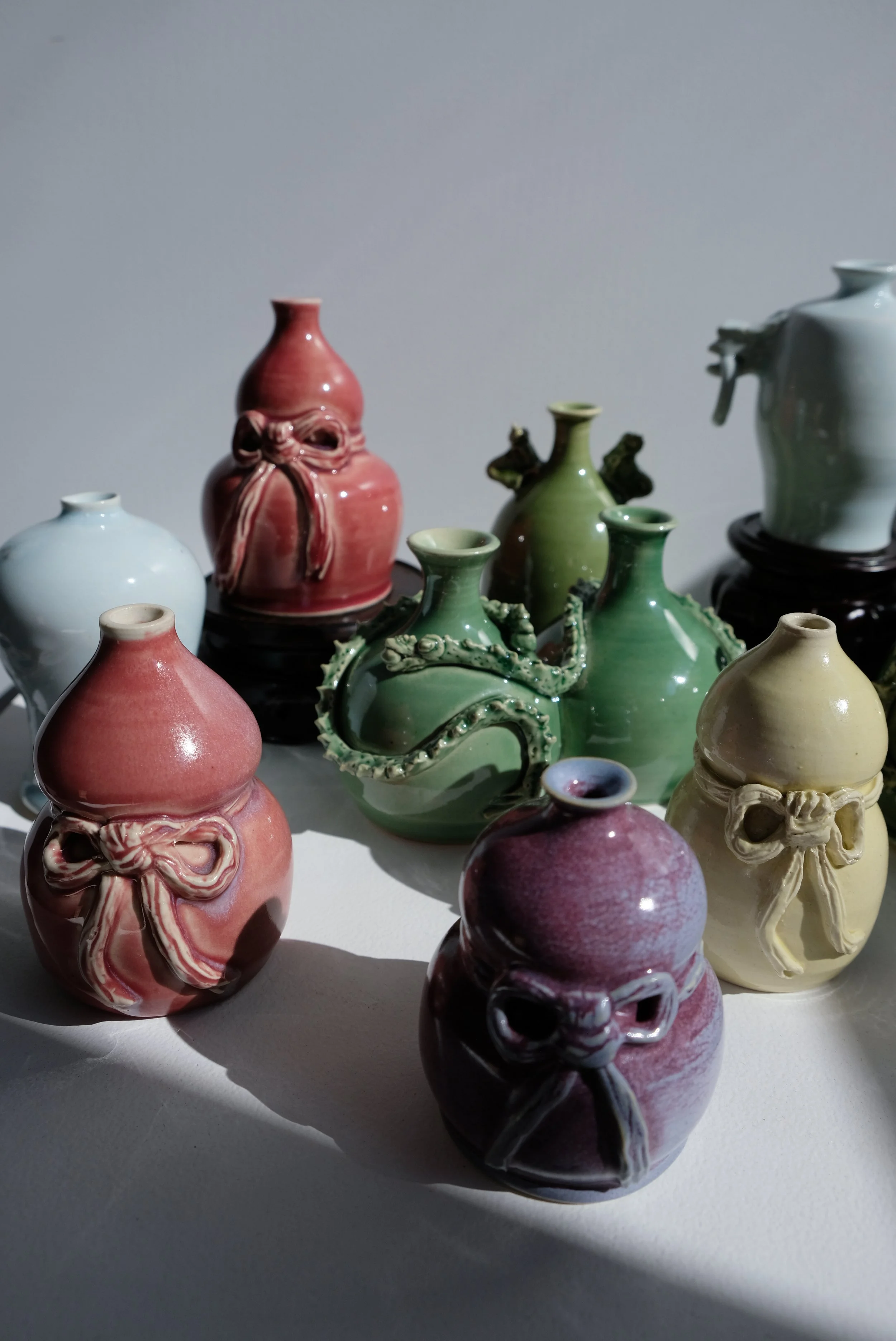 Collection of colorful ceramic vases, some with bows and others with dragon or octopus motifs, on a white surface with shadows.