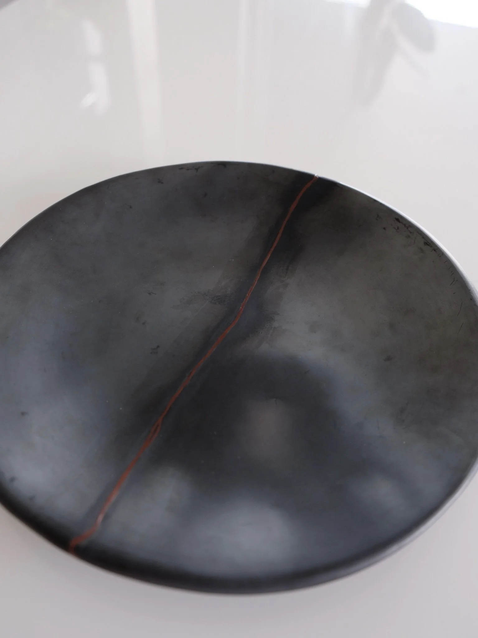 Close-up of a dark, round, shallow bowl with a red line running along the center, placed on a white surface.