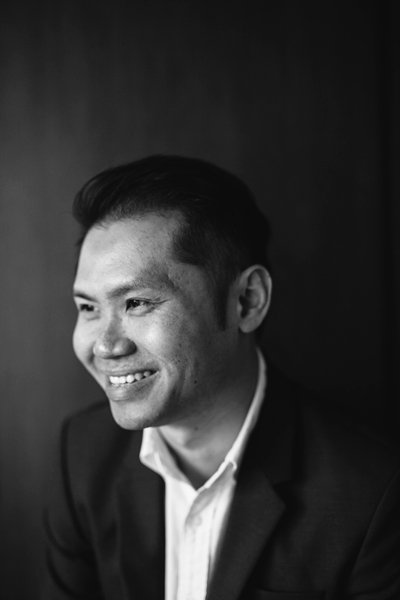 Black and white portrait of a smiling man in a suit, looking to the left, against a dark background.
