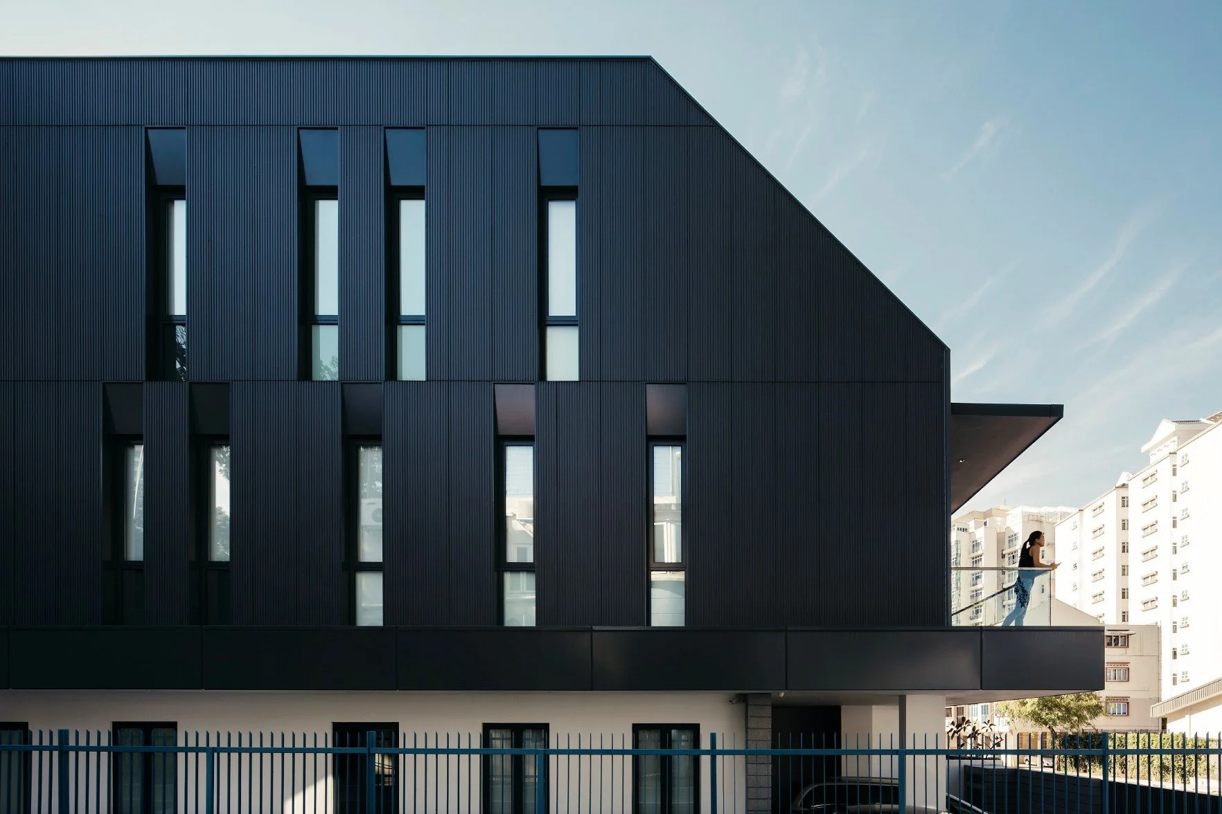 Modern house with a dark textured façade, vertical patterning, and tall slit windows that accentuate its sculptural form. A projecting balcony overlooks a busy street in Singapore and connecting the residence to its urban context.