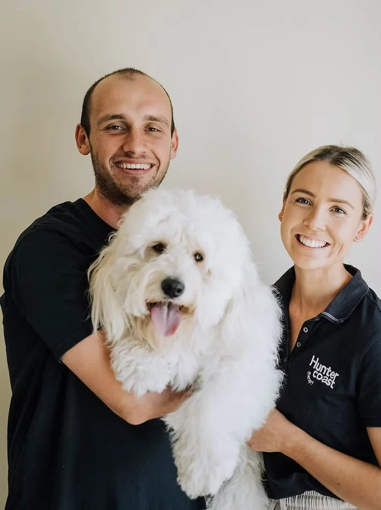 A man and a woman smiling while holding a fluffy white dog together.