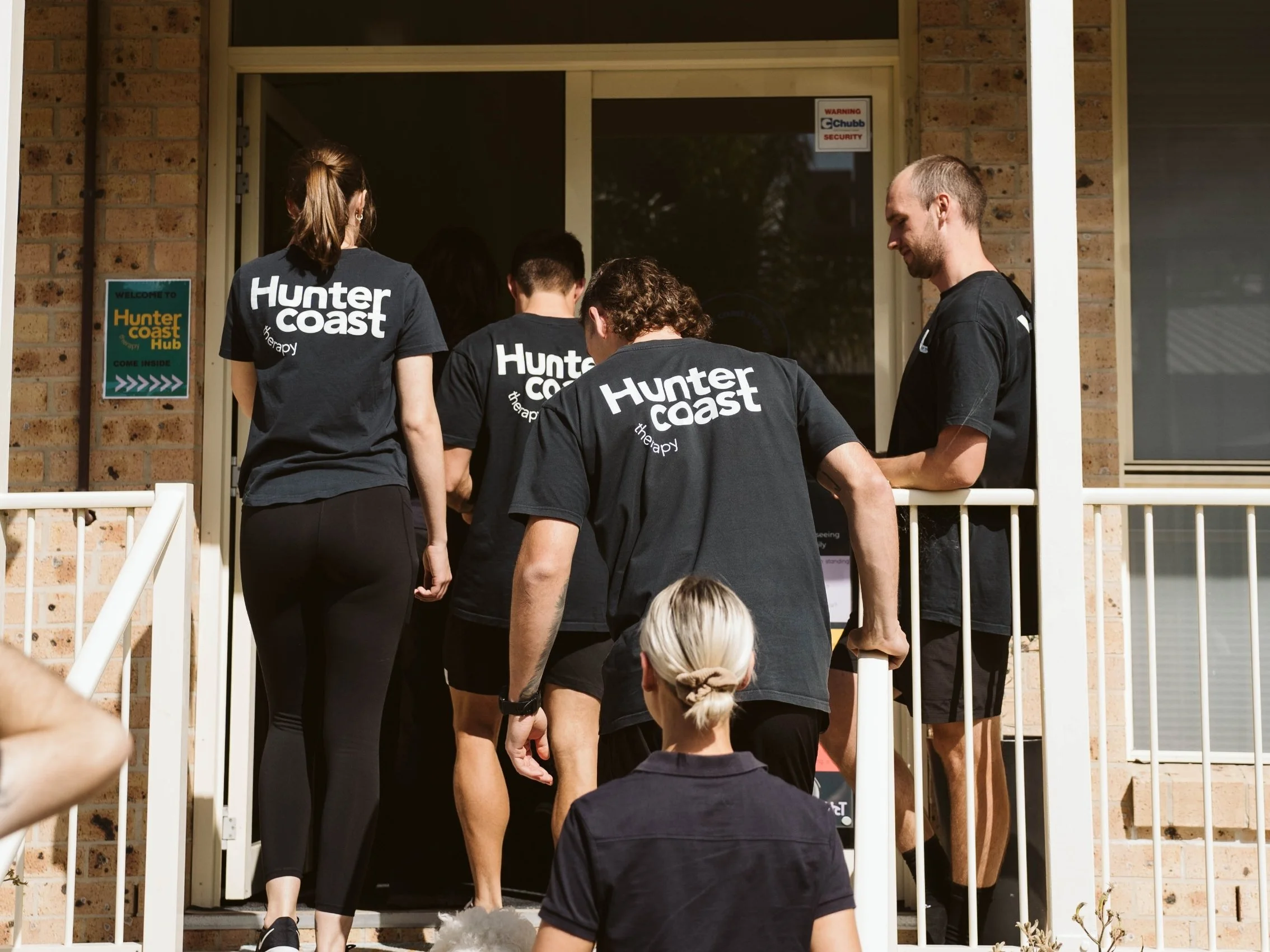 four people walking up stairs to the entry of a building all wearing the same hunter coast therapy shirt