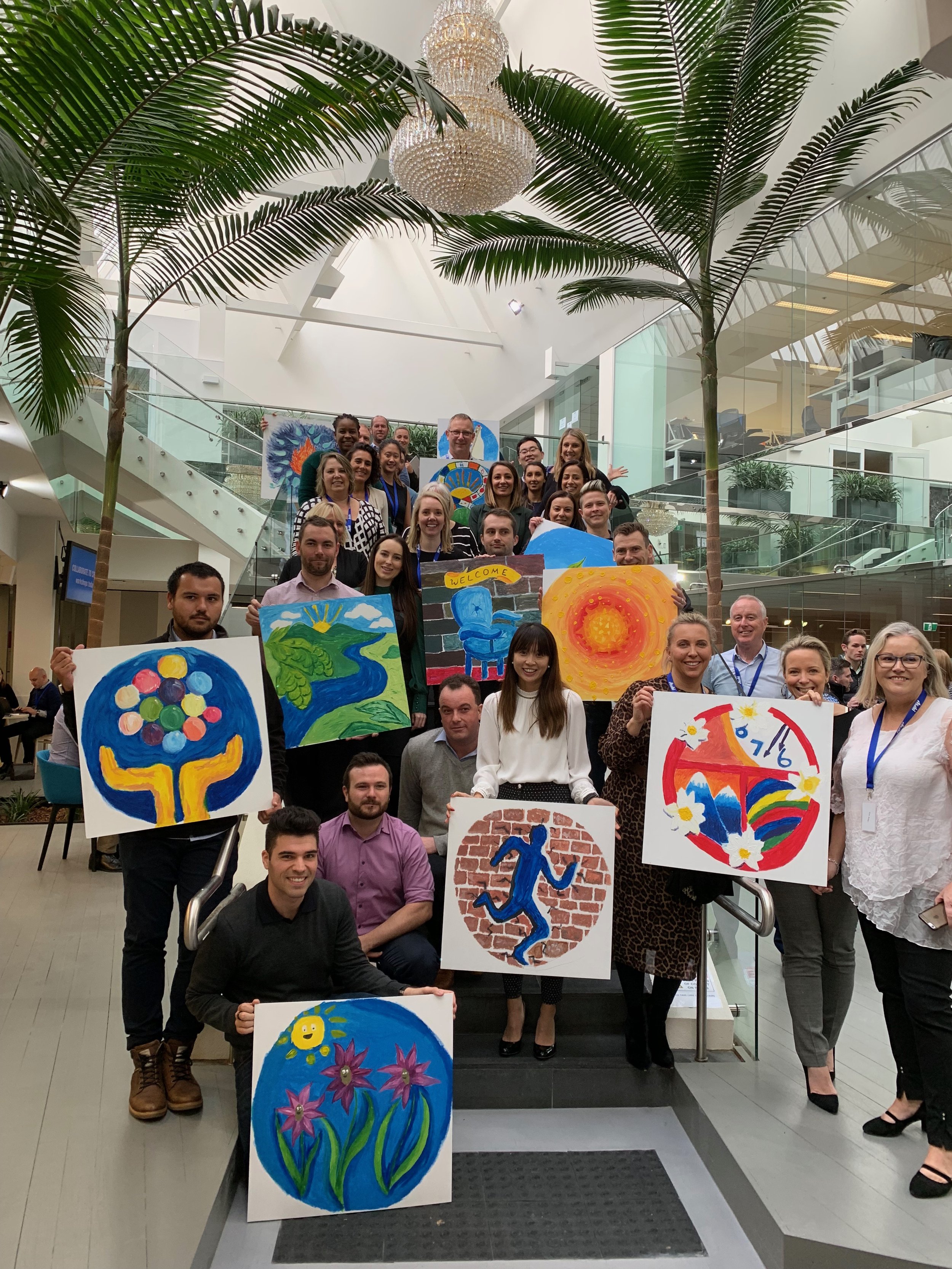 Corporate team development workshop participants showcasing thier paintings and connecting during a Mind Gallery team mural experience.