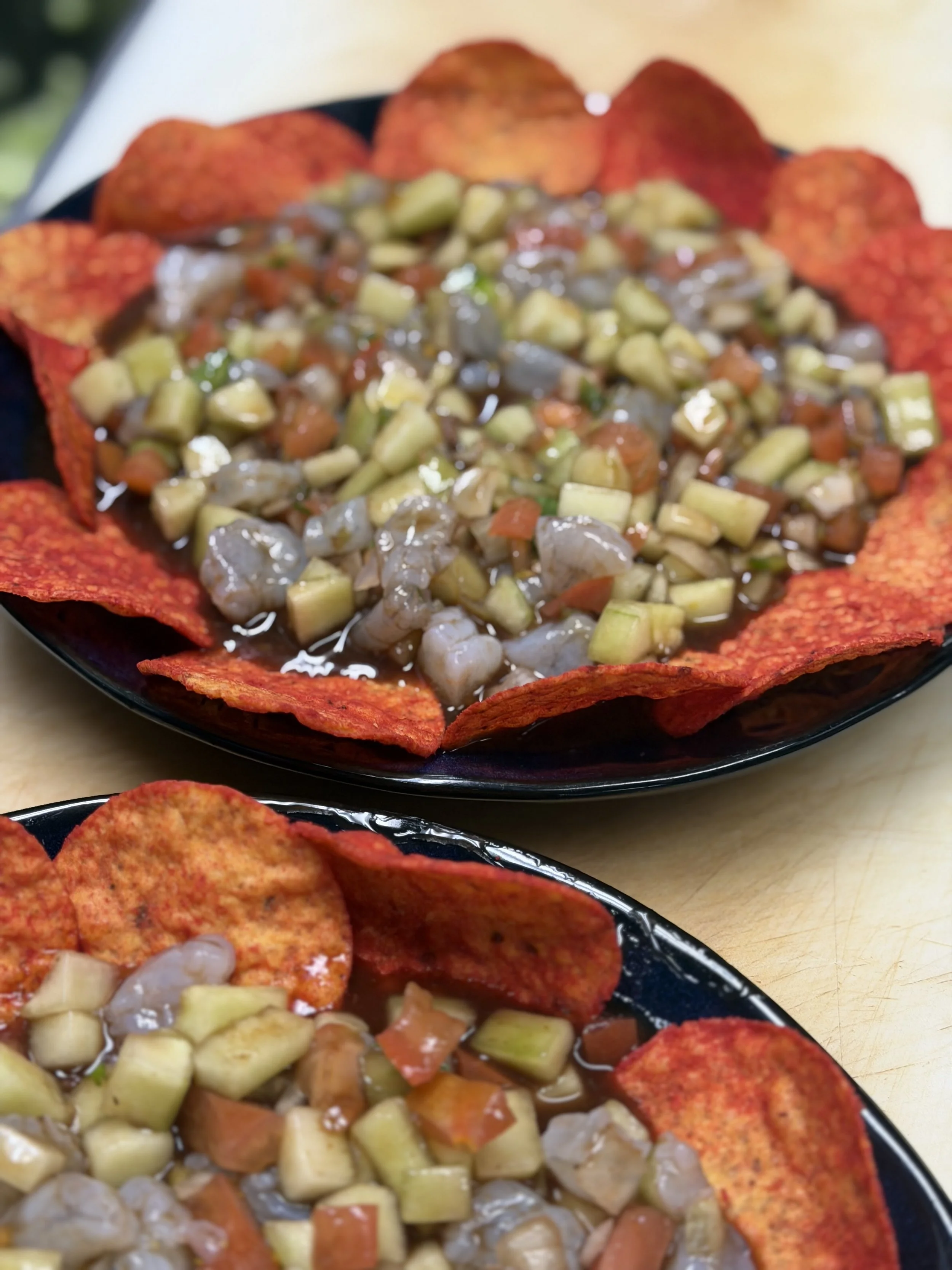 A plate of nachos topped with diced vegetables and shredded cheese, surrounded by spicy red tortilla chips.
