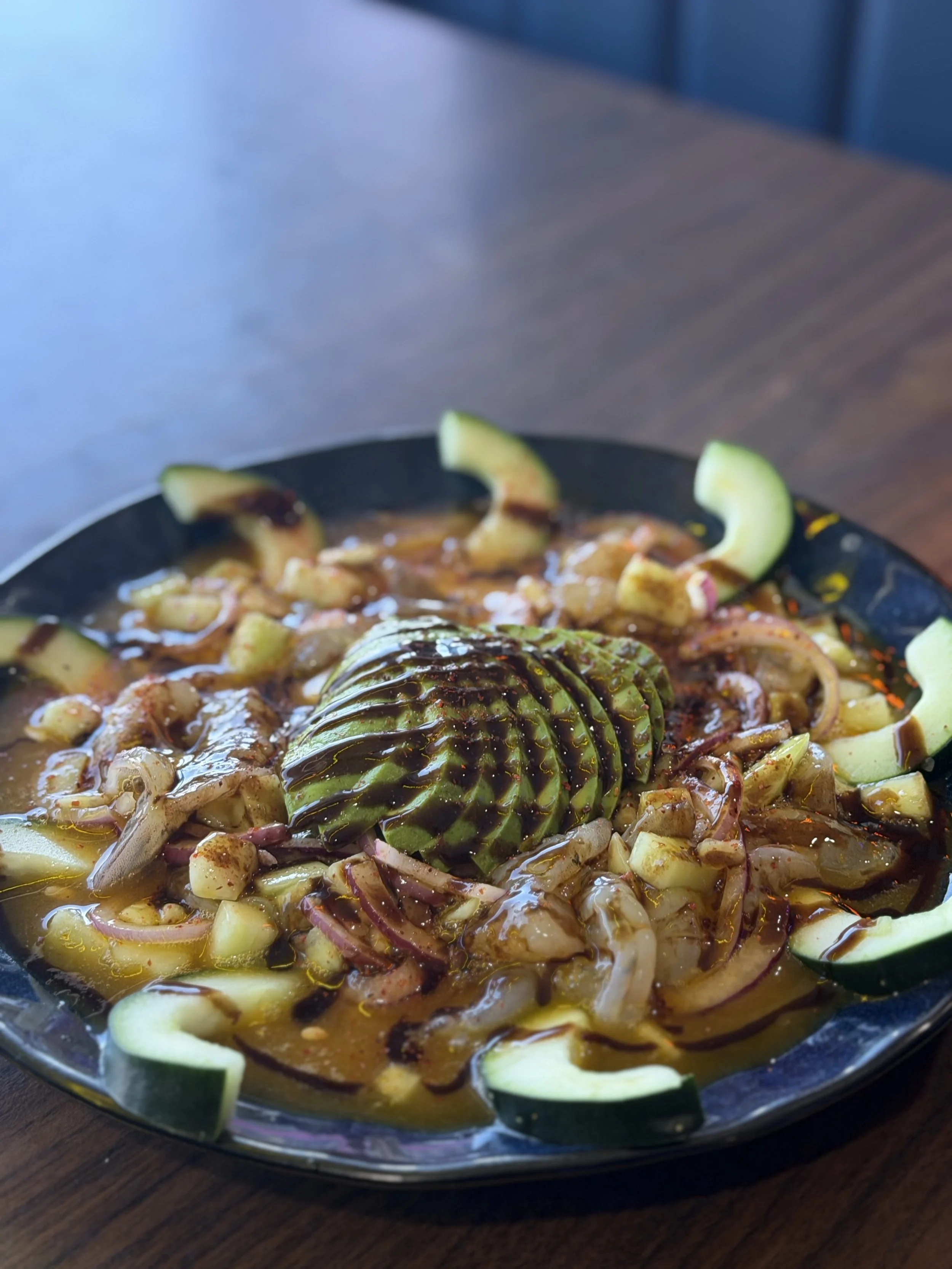 A bowl of Mexican food with rice, grilled vegetables, and topped with steak and sliced avocado.