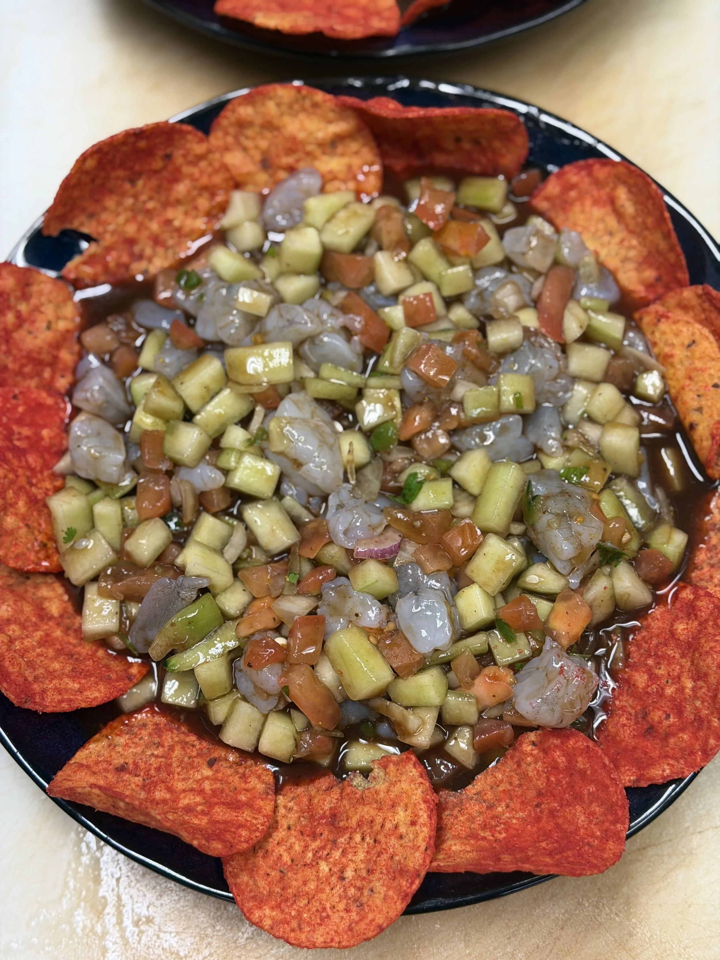 Plate of shrimp ceviche topped with diced cucumbers and chopped vegetables, surrounded by red papadum chips.