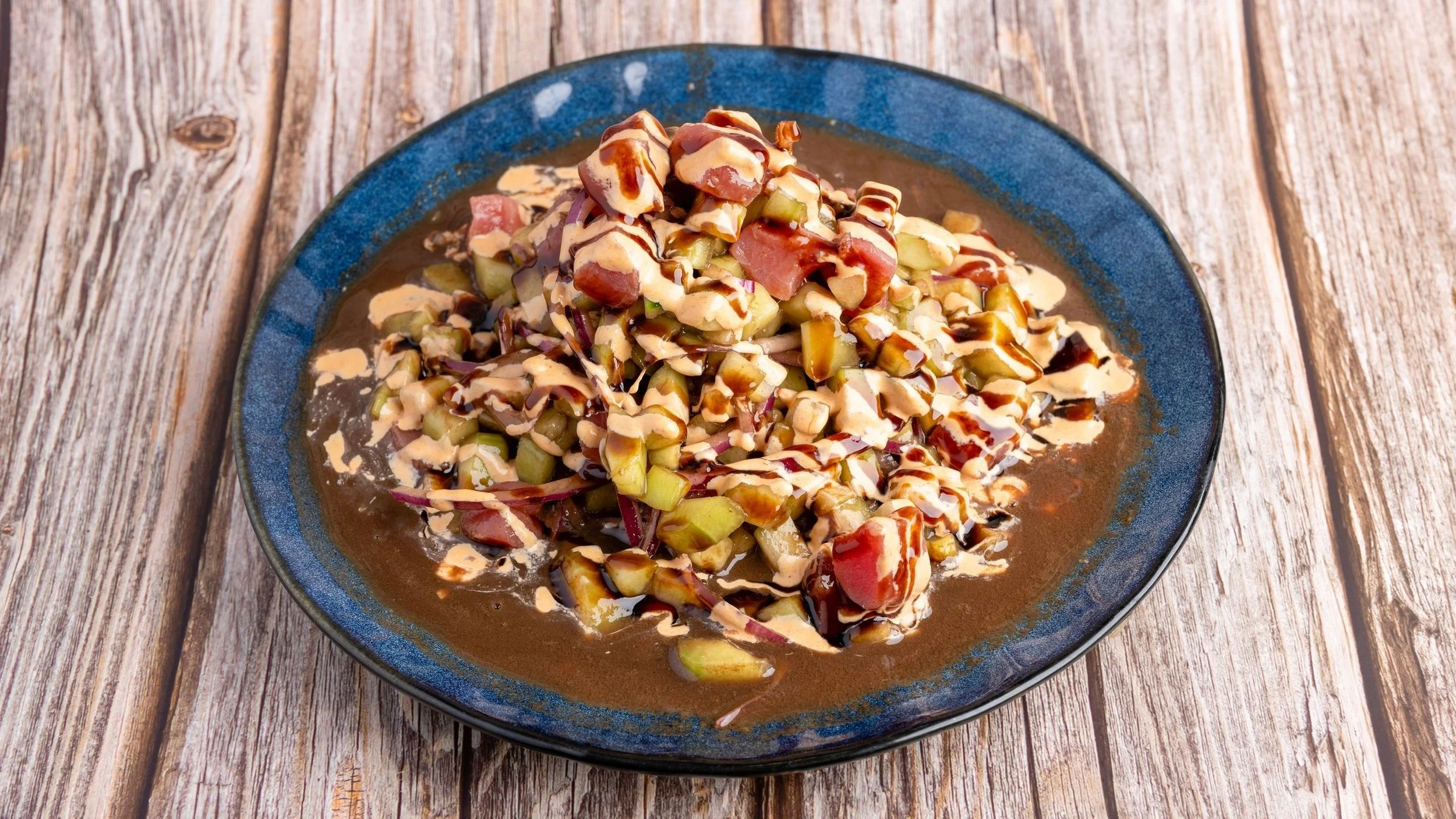 A plate of chopped vegetables topped with sauces on a wooden table.