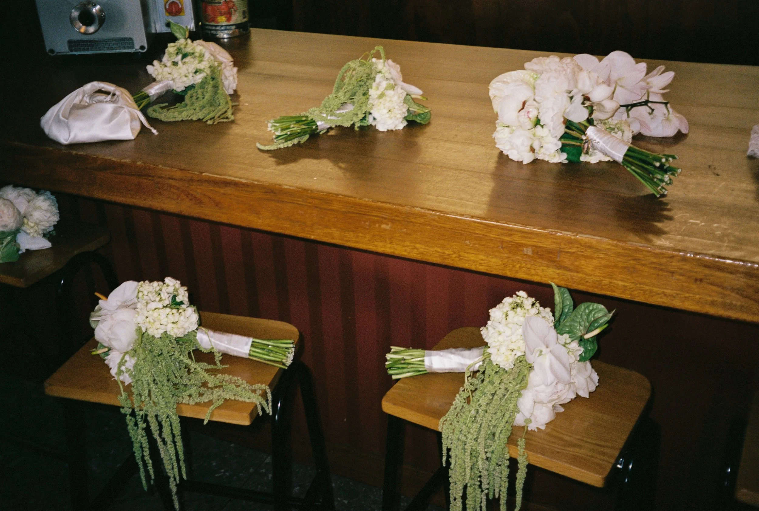 Several bridal bouquets and flower arrangements placed on a wooden counter and chairs, likely prepared for a wedding ceremony.