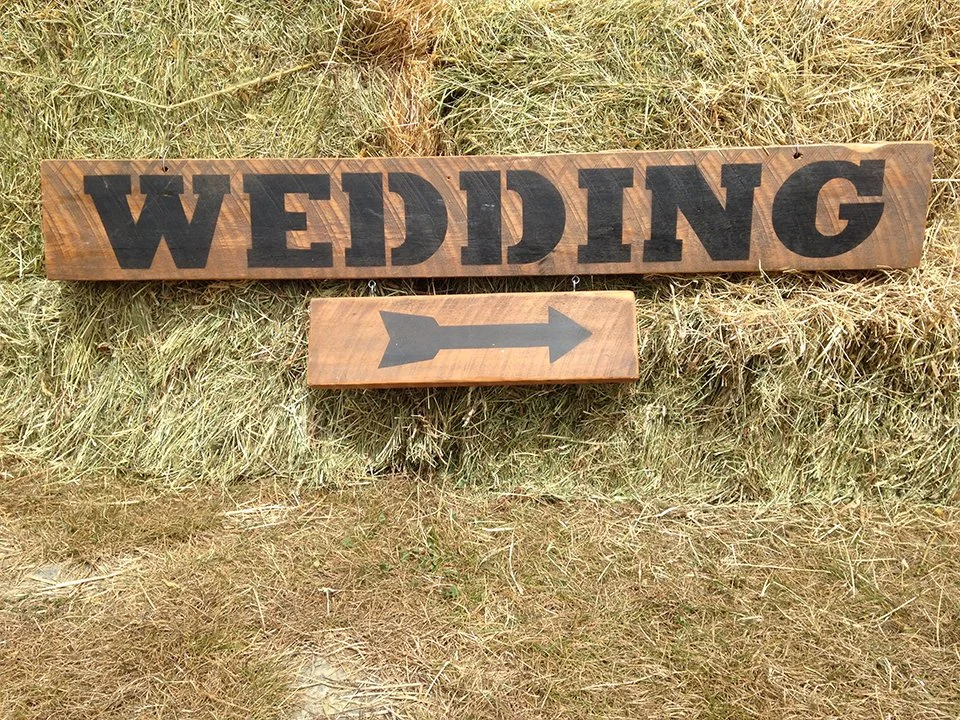 Wooden wedding sign with a large arrow pointing to the right, placed on grass.